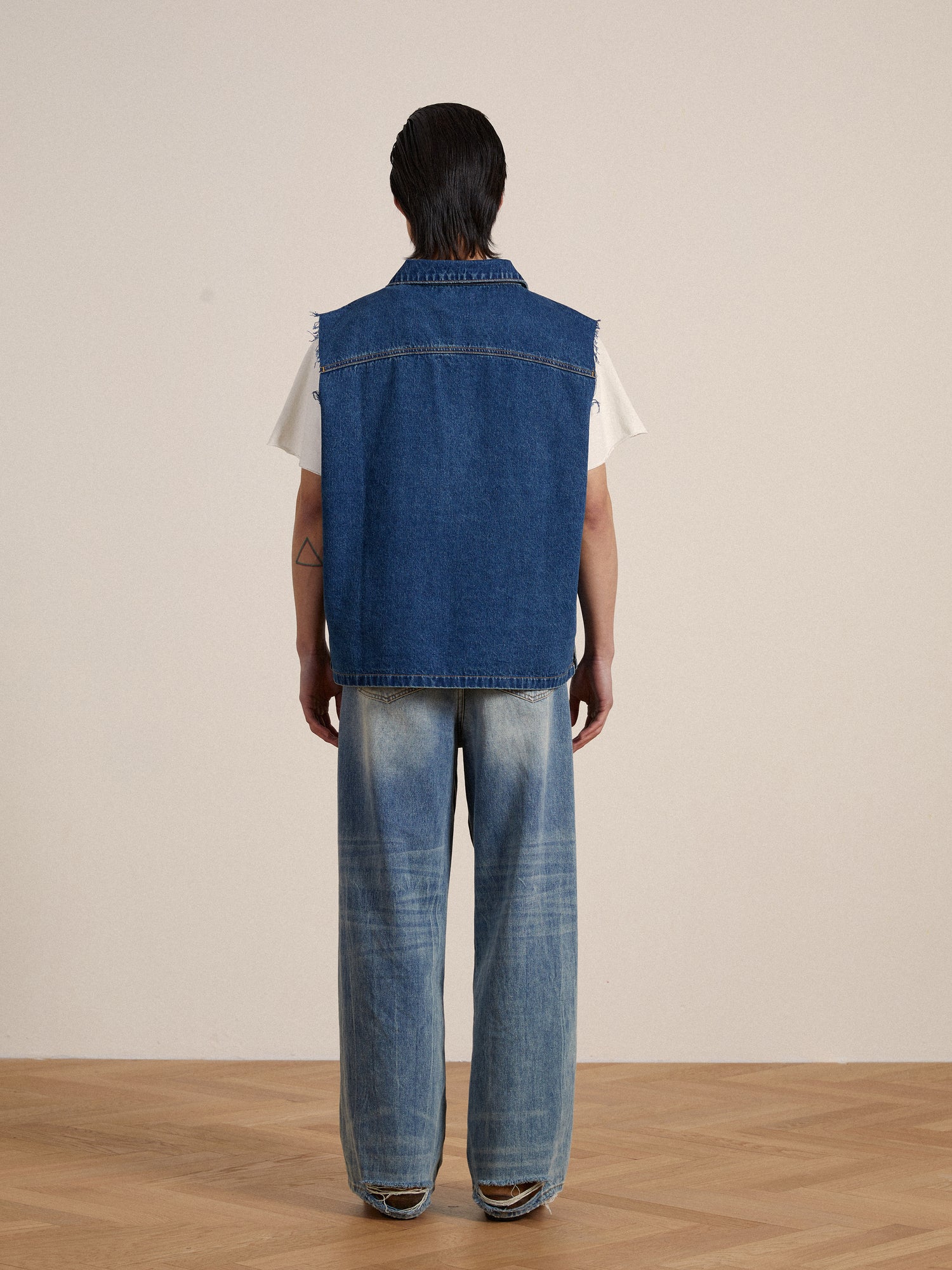 The back view of a man wearing a Found Raw Cut Patch Mechanic Denim Vest with embroidered patches.