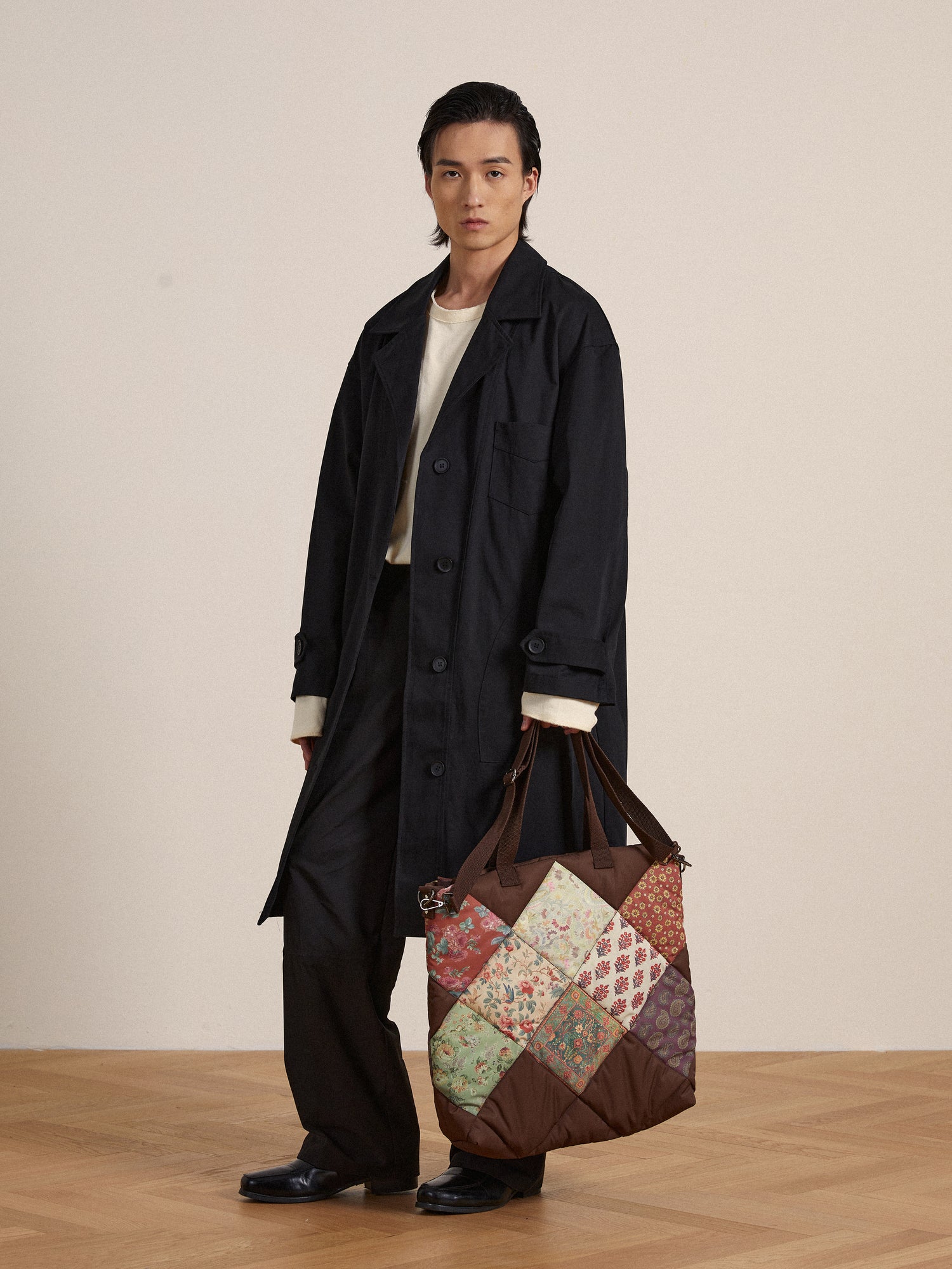 A man in a black coat holding a Profound Parisa Quilted Tapestry Bag.
