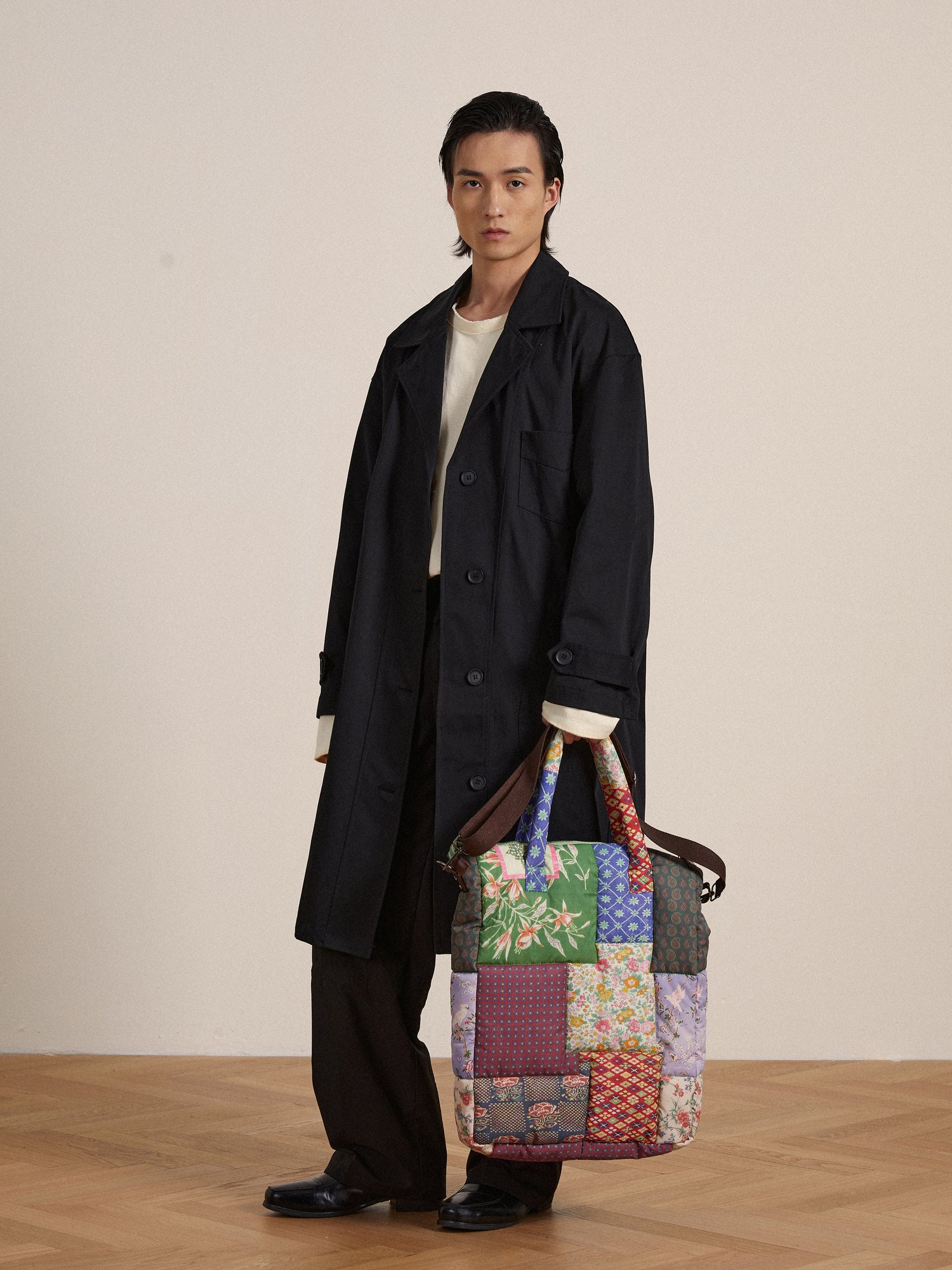 A man in a trench coat holding a Profound Gardenia Tapestry Bag.