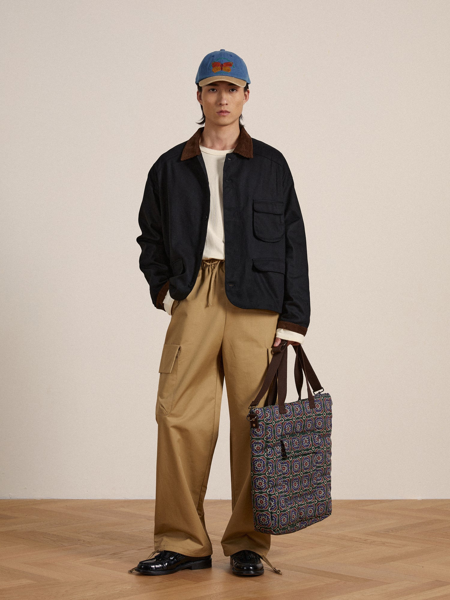 A man is holding a Lar Waxed Cotton Box Coat tote bag by Found in front of a wooden floor.