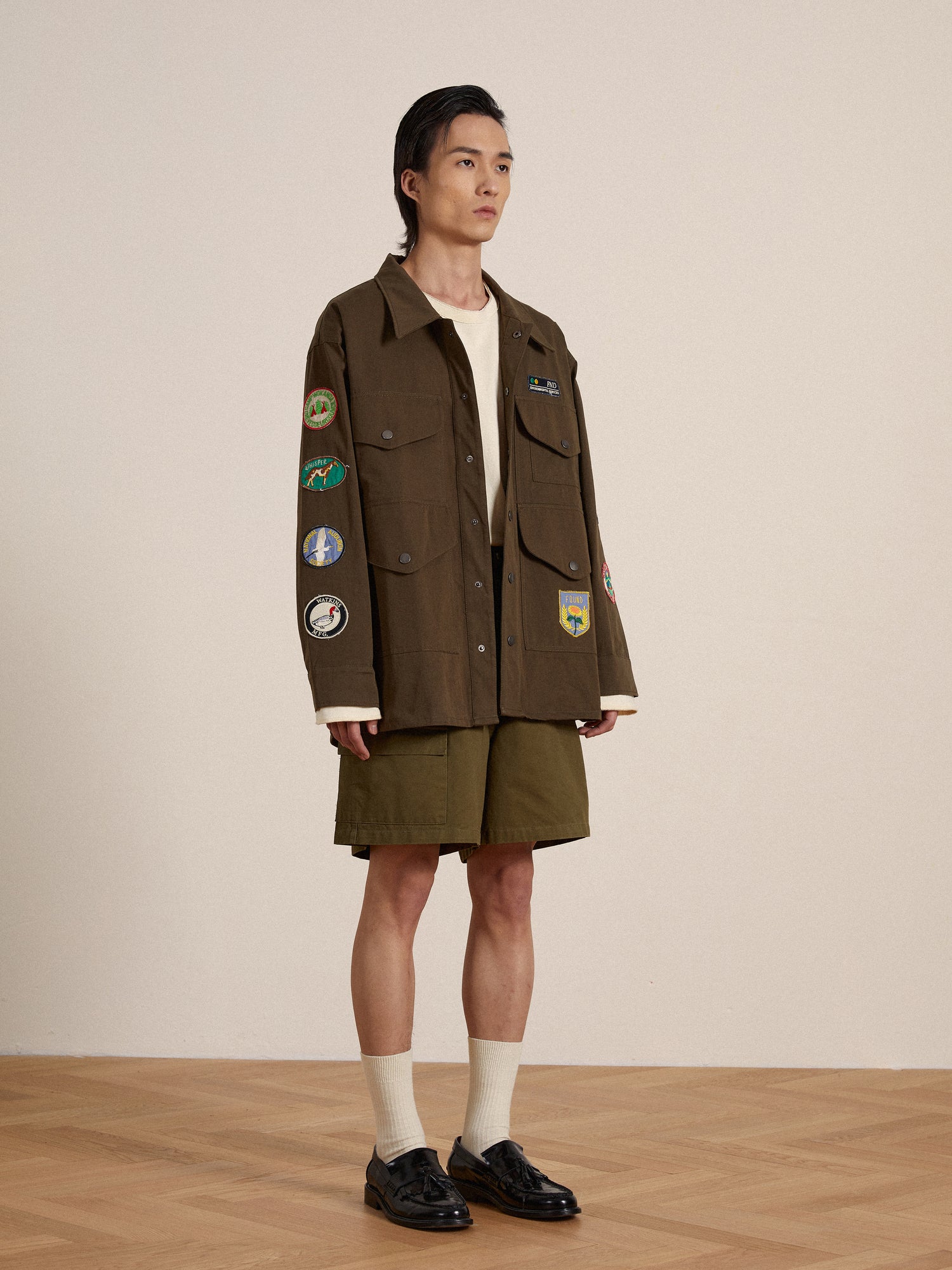 A man wearing a vintage-inspired Found Ports Park Multi Patch Work Jacket with embroidered patches and shorts.