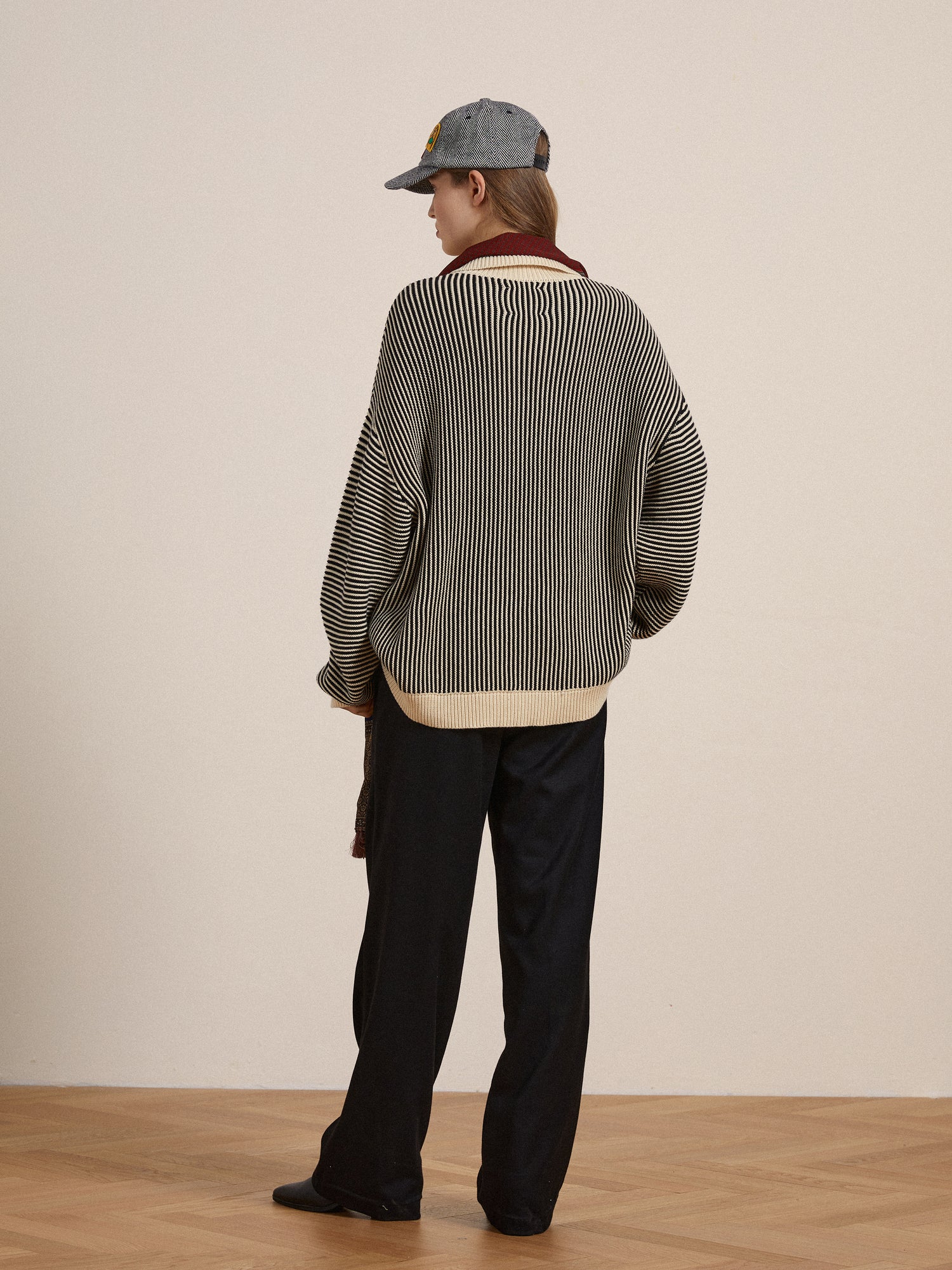 The back view of a woman wearing a grey Found Tabas Tie Knit Collared Sweater with intricate knit patterns and black pants.