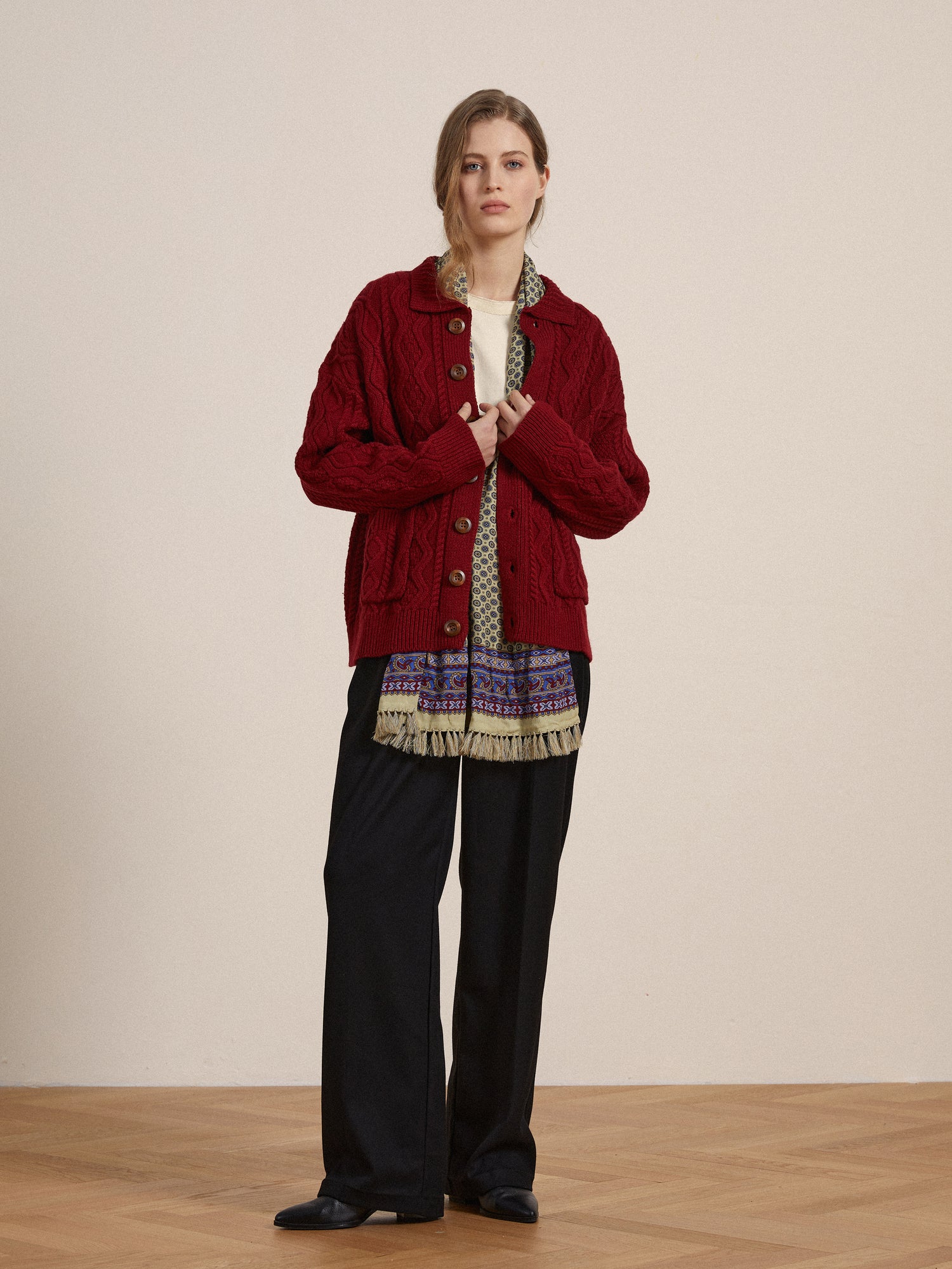 A woman wearing a red-hued Found Parsidan cable knit cardigan and black pants.