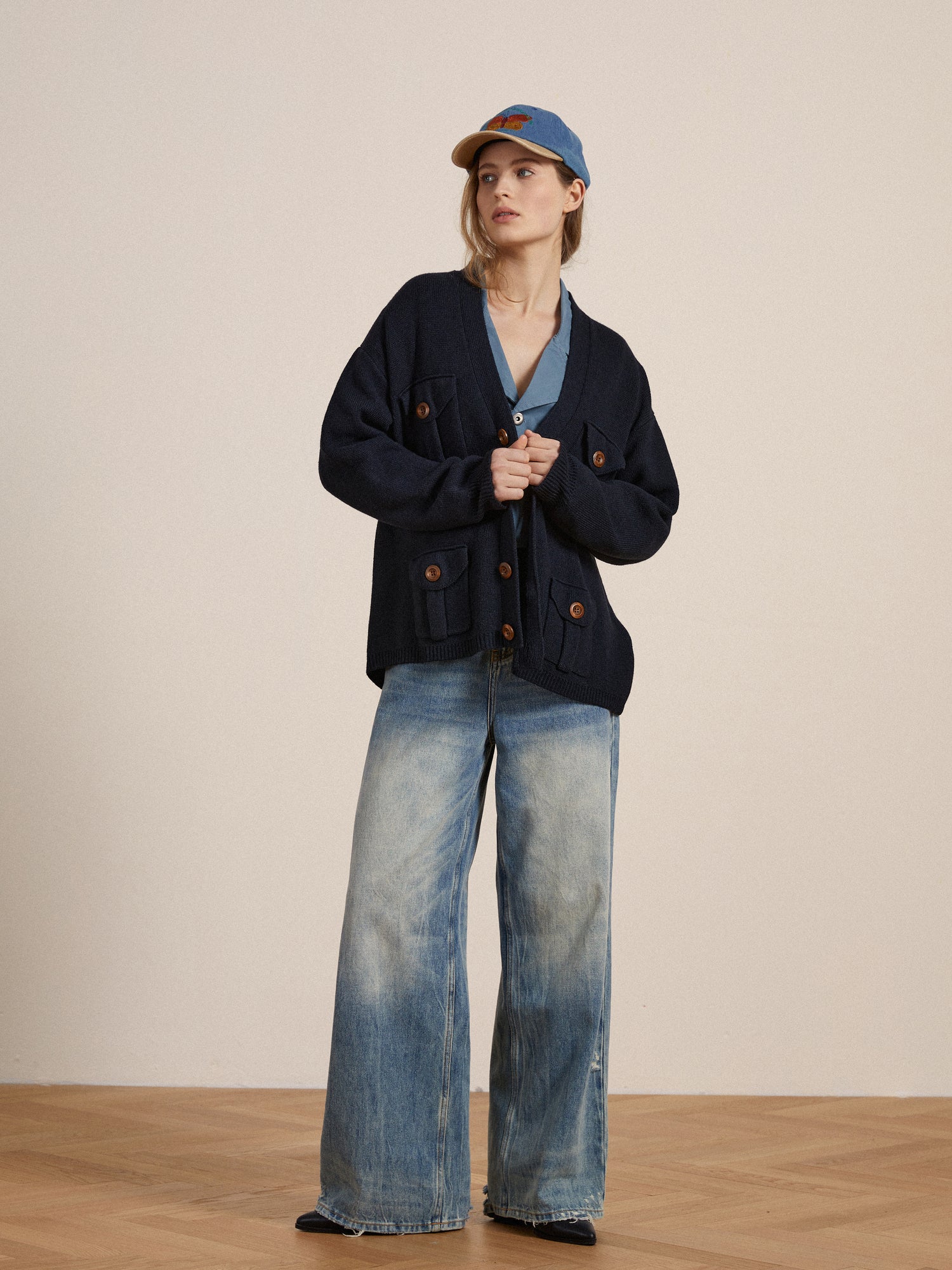A woman wearing a blue Found Multi Pocket Cardigan and wide leg jeans.