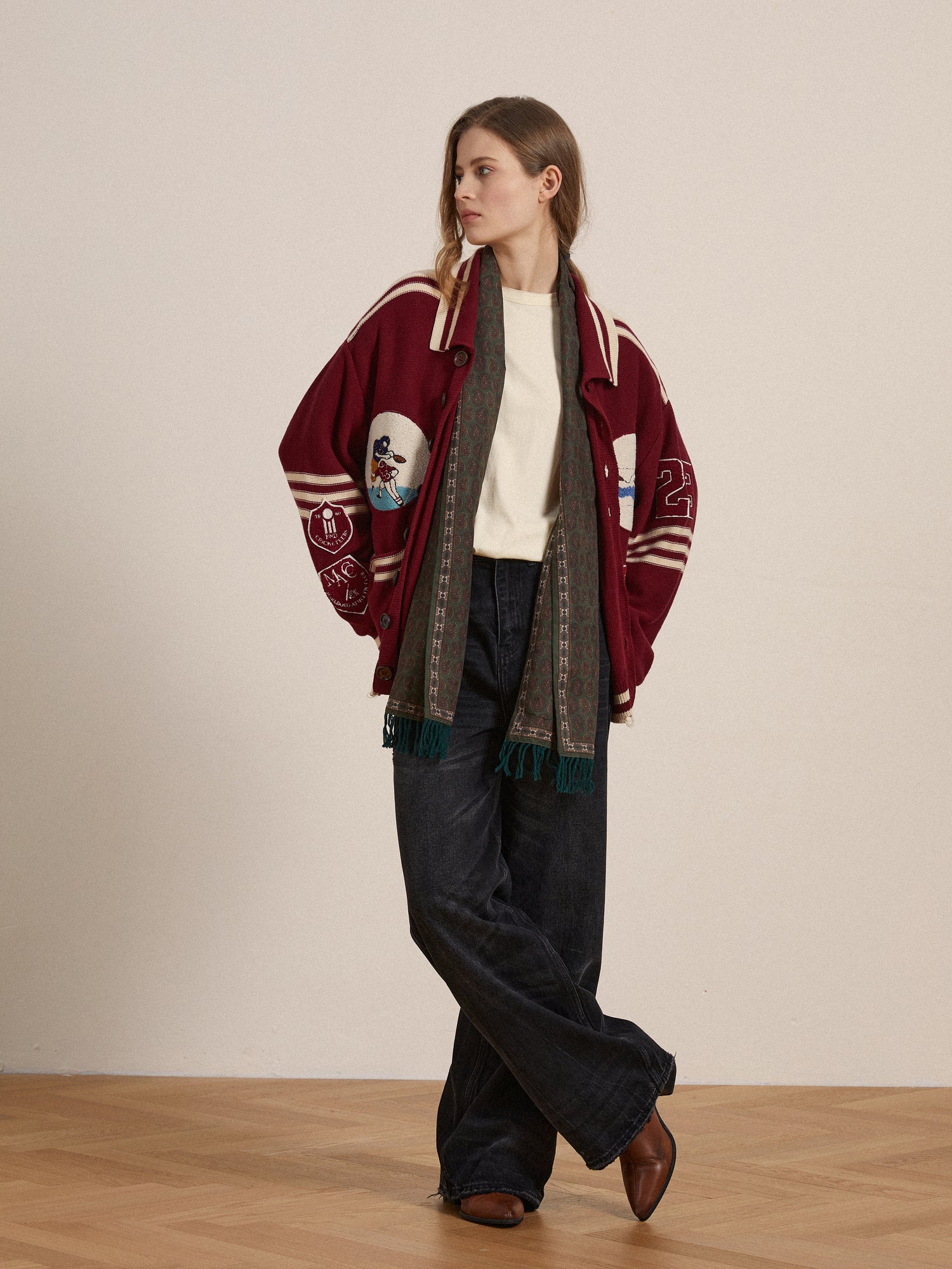 A woman wearing a burgundy Found Fin Varsity Patch Collared cardigan and scarf, adorned with embroidered chenille patches.