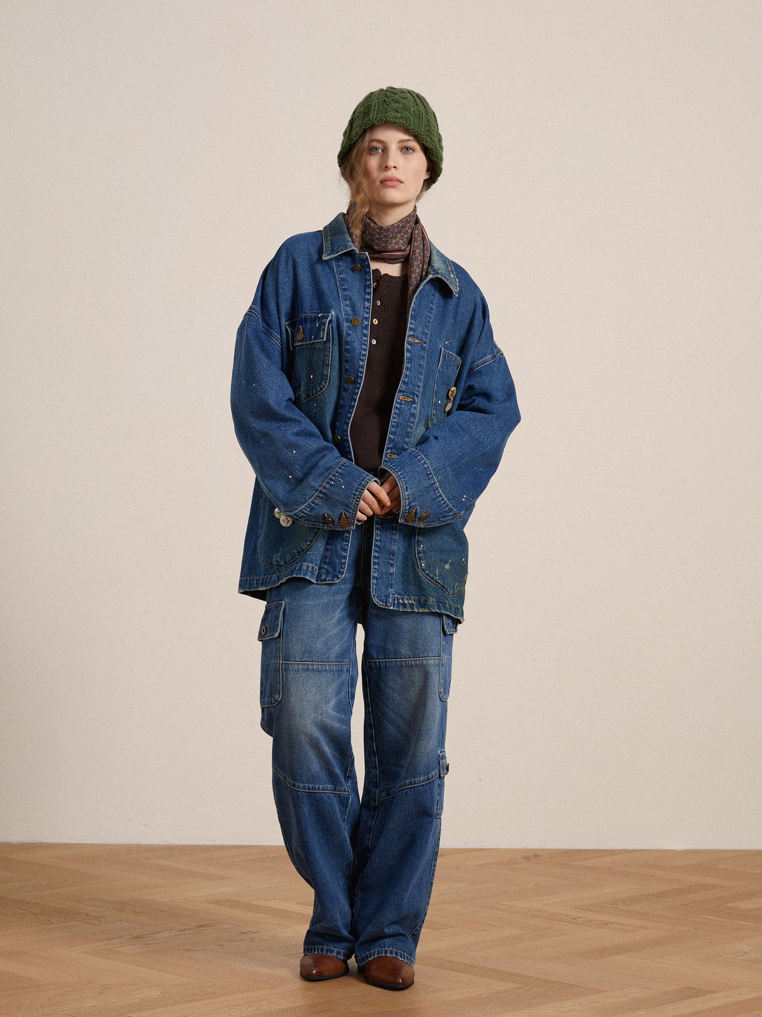 A woman in a Kavir Denim Painter Jacket and green hat standing on a wooden floor by Found.