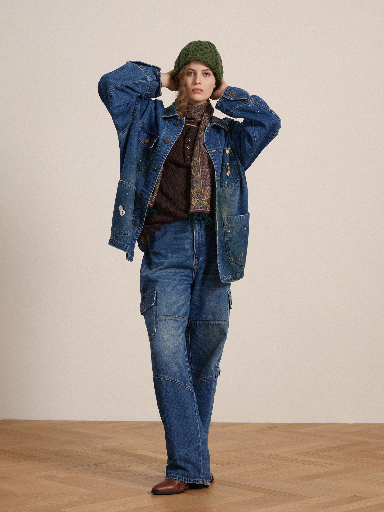 A woman in a stylish denim outfit, featuring a jacket, Siwa Cargo Paneled Jeans, and a green beanie, stands against a neutral background.