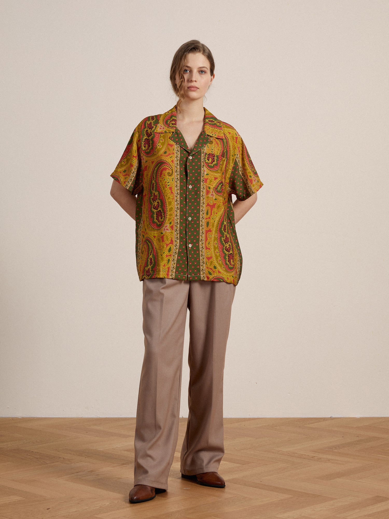 A woman wearing a yellow Pench Paisley SS Camp Shirt by Found and beige pants.
