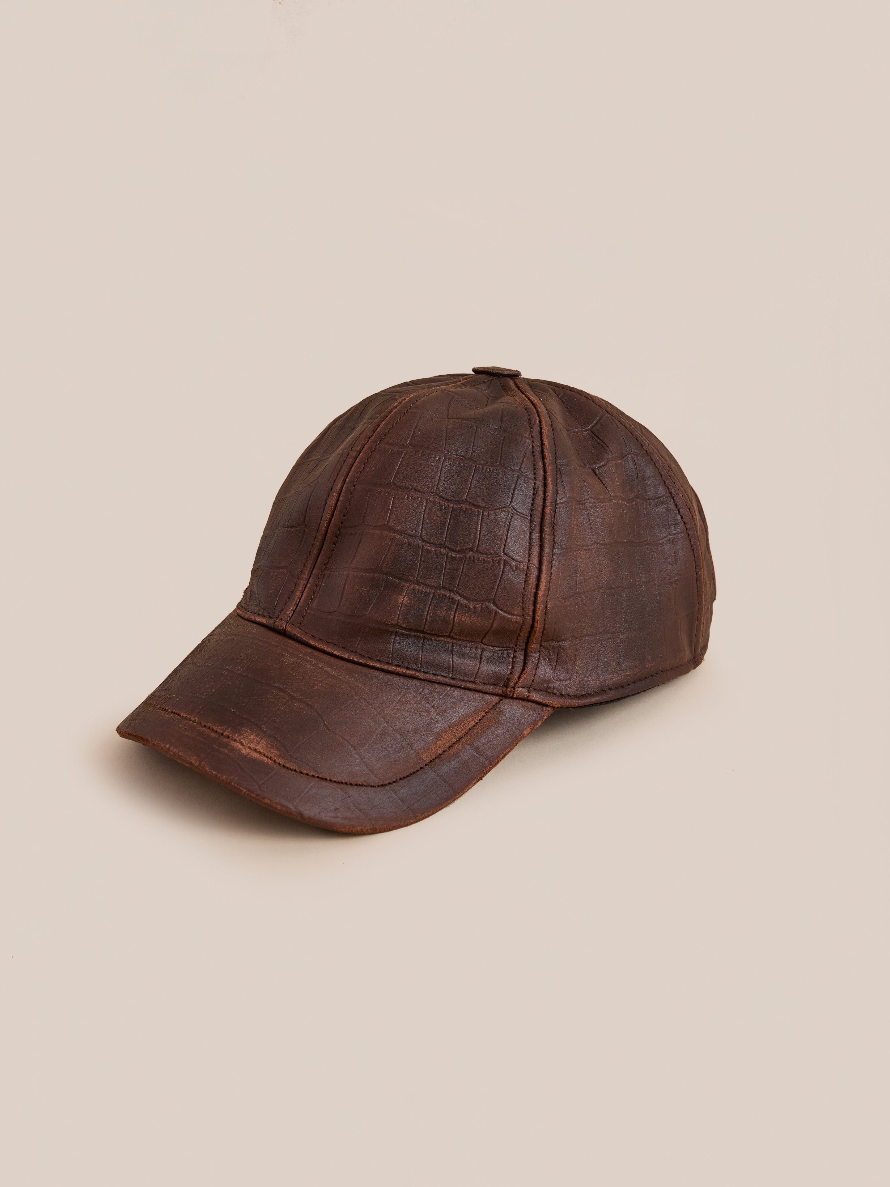The Found Croc Embossed Distressed Leather Cap, featuring a brown crocodile-patterned finish, is showcased on a neutral beige background.