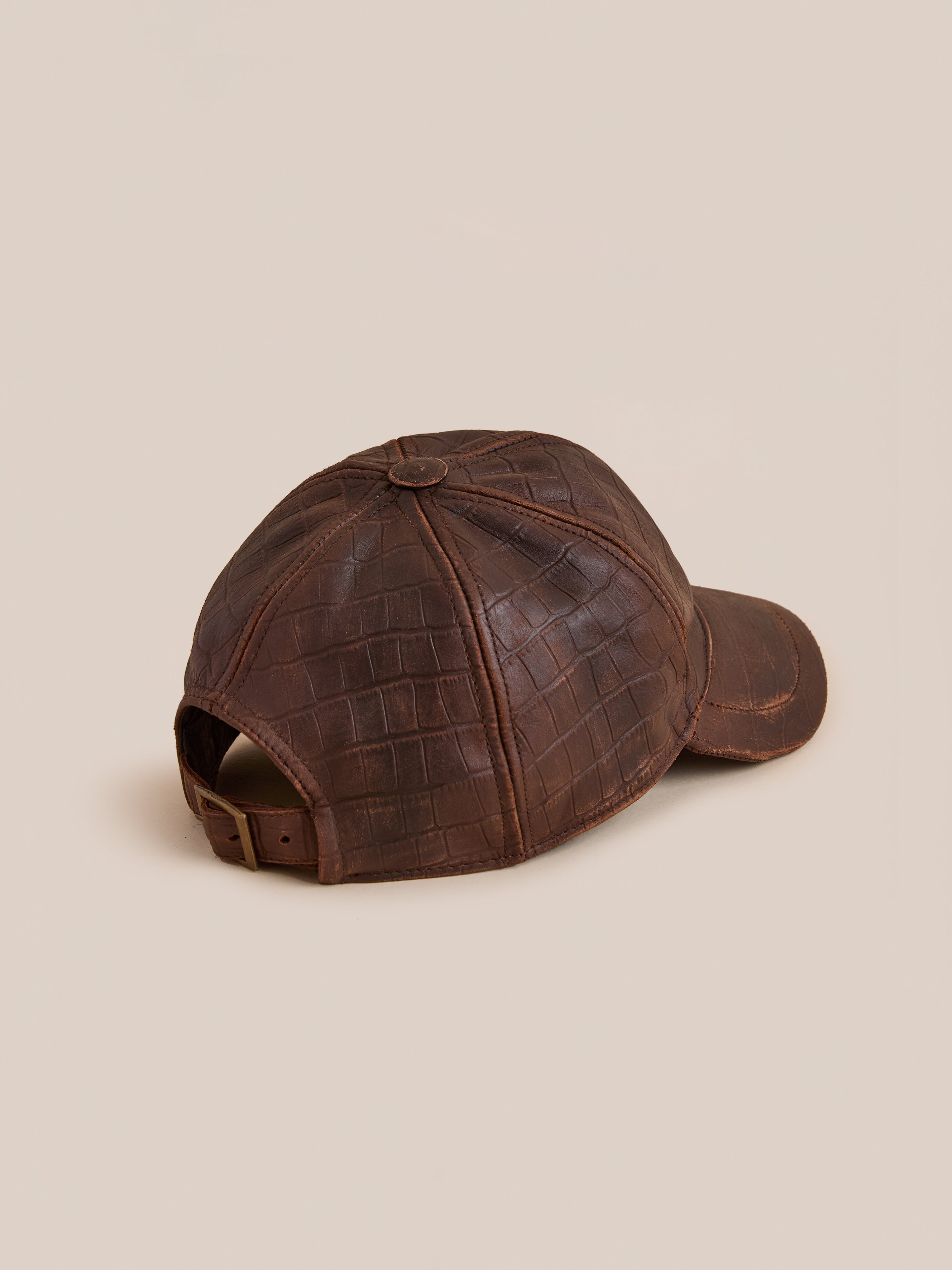 Found Croc Embossed Distressed Leather Cap in brown leather with an adjustable strap and curved brim, shown from the back on a beige background.