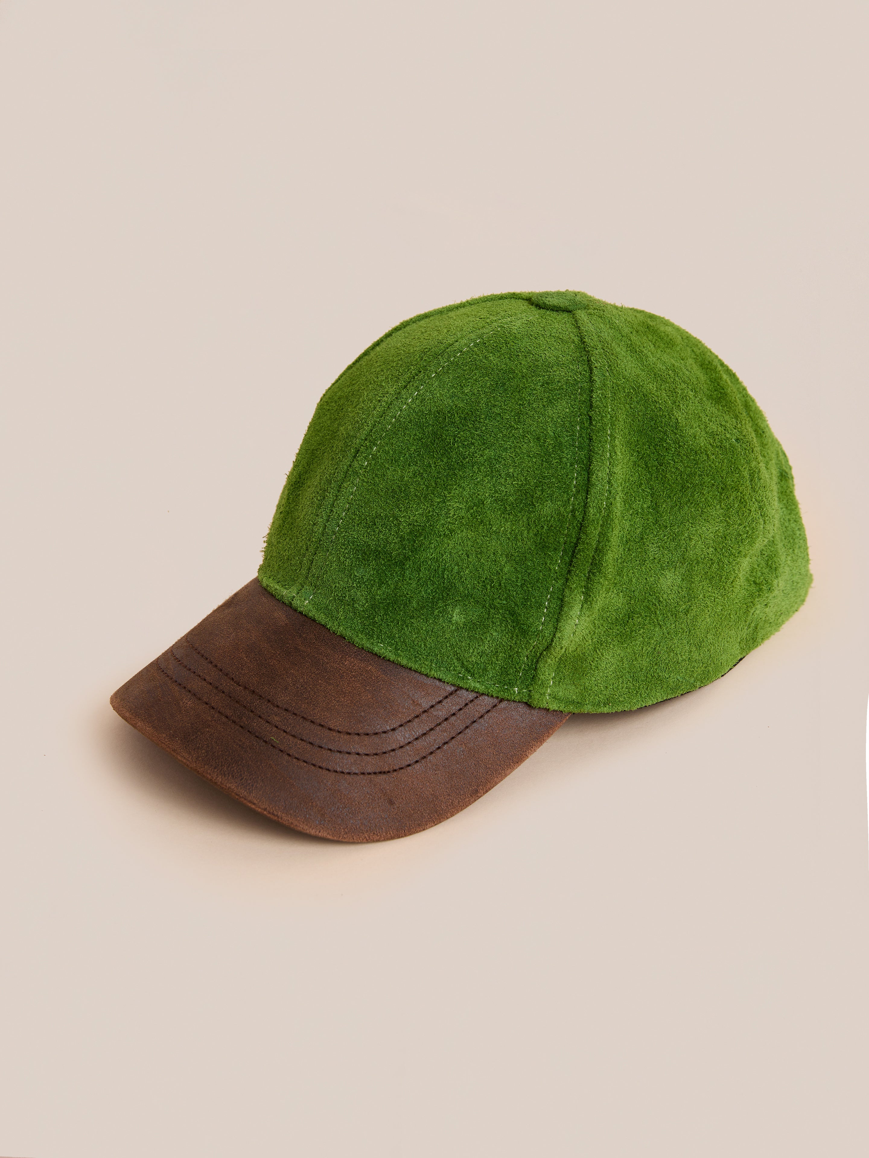 The Found Suede Leather Contrast Distressed Cap features green suede, a distressed brown leather brim, and an adjustable leather strap, shown against a neutral background.