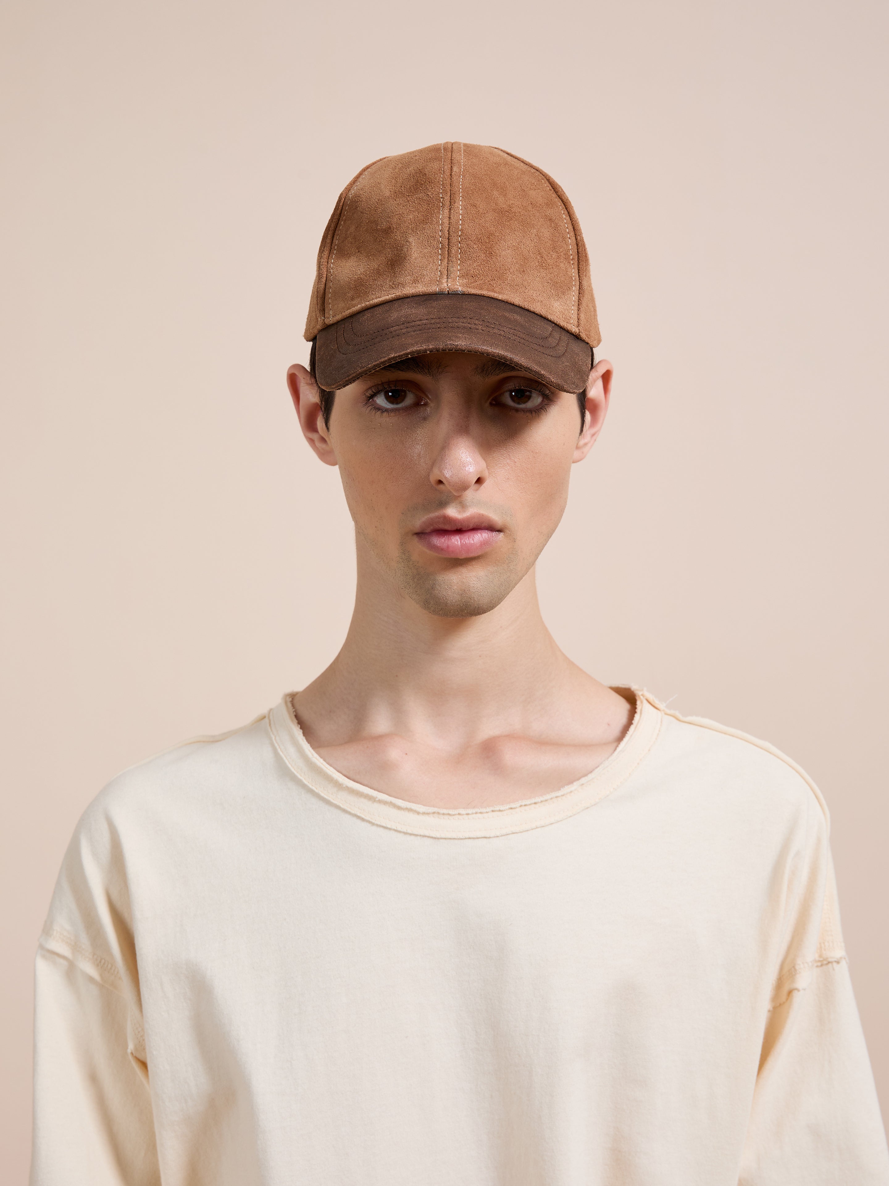 Against a plain beige background, a person wears the Found Suede Leather Contrast Distressed Cap and an off-white T-shirt.