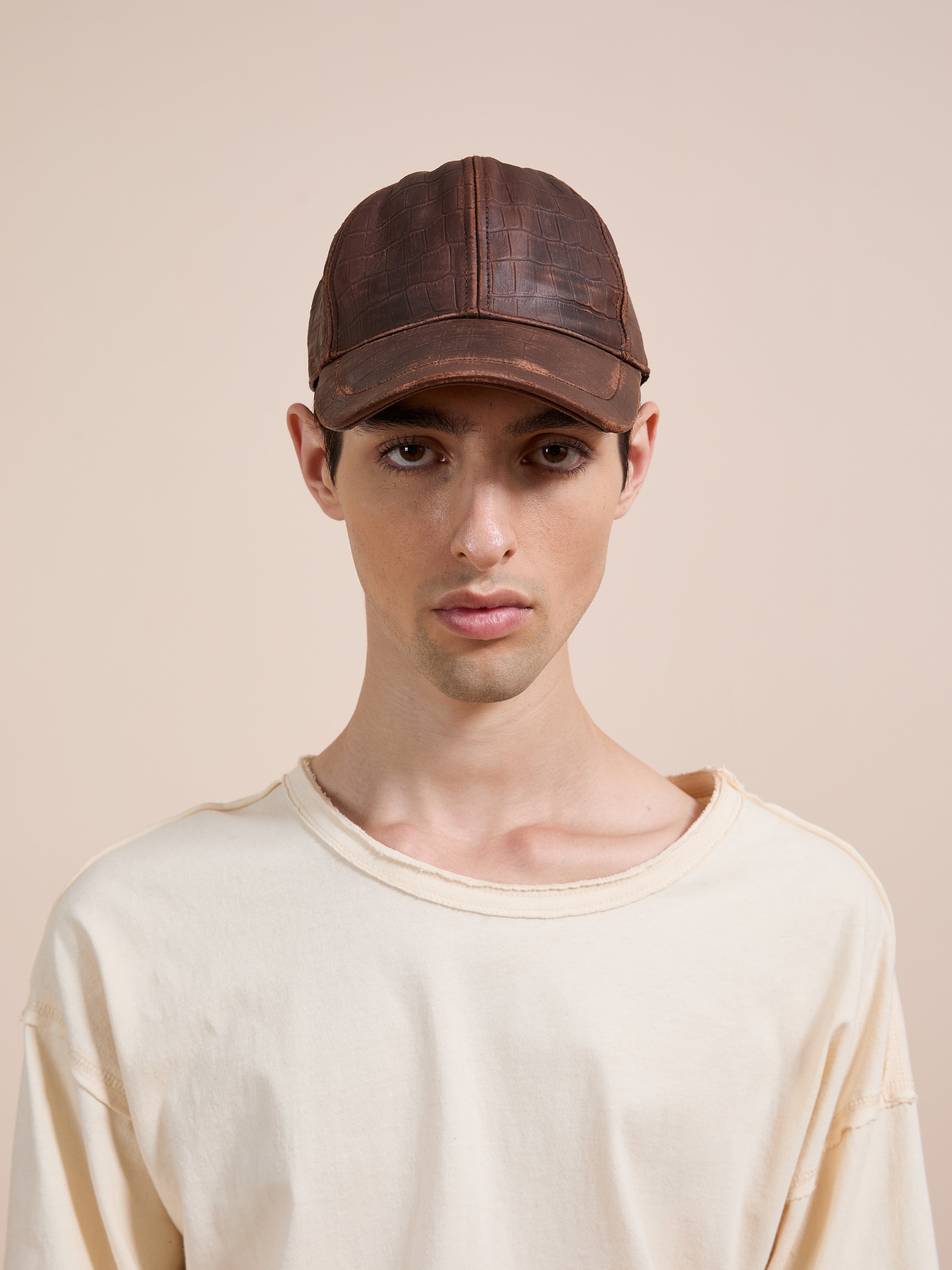 A person wears the Found Croc Embossed Distressed Leather Cap with a cream, slightly frayed t-shirt, facing forward against a plain beige background.