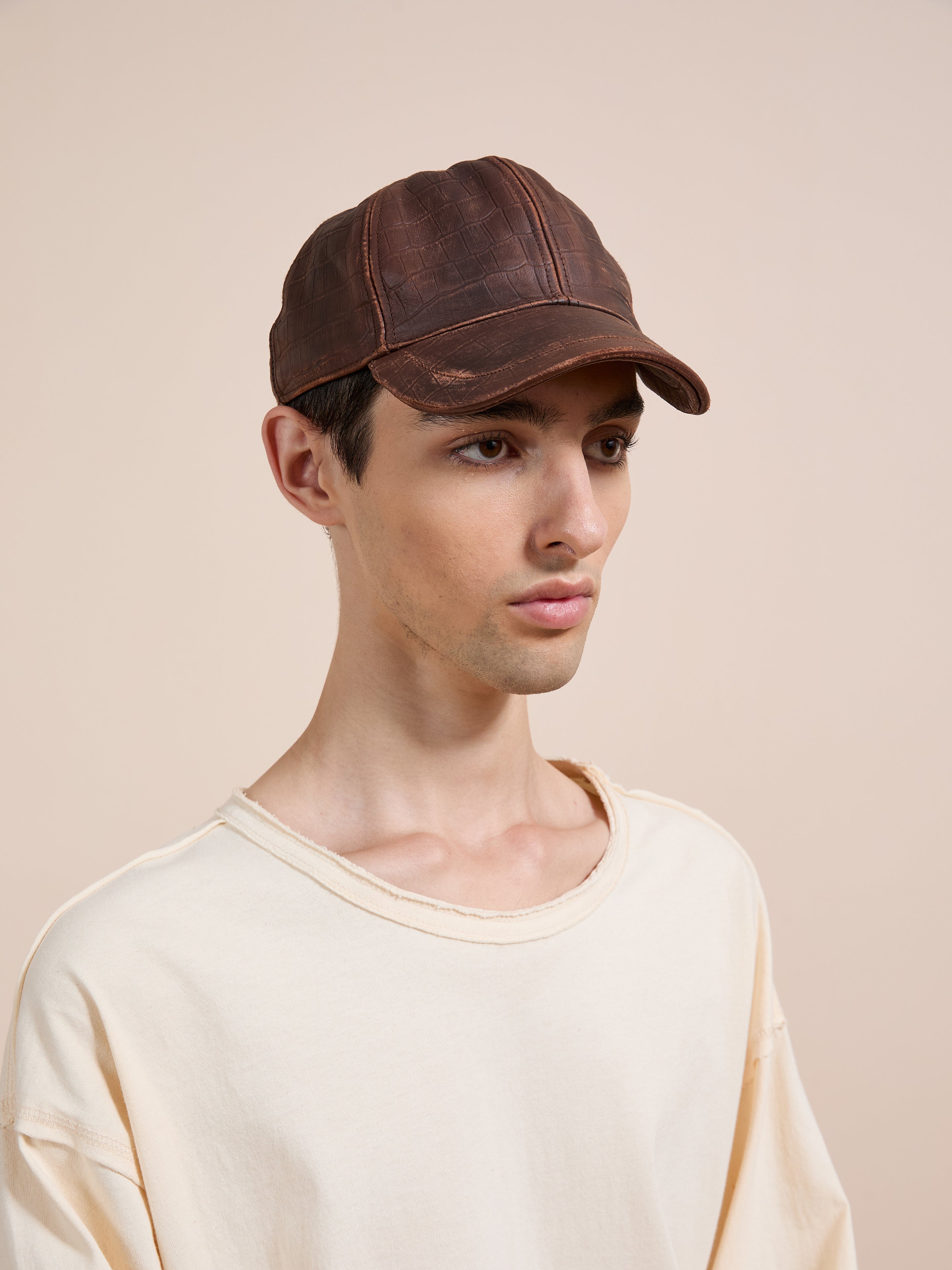 A young person wears the Found Croc Embossed Distressed Leather Cap and an off-white t-shirt, standing against a plain beige background.