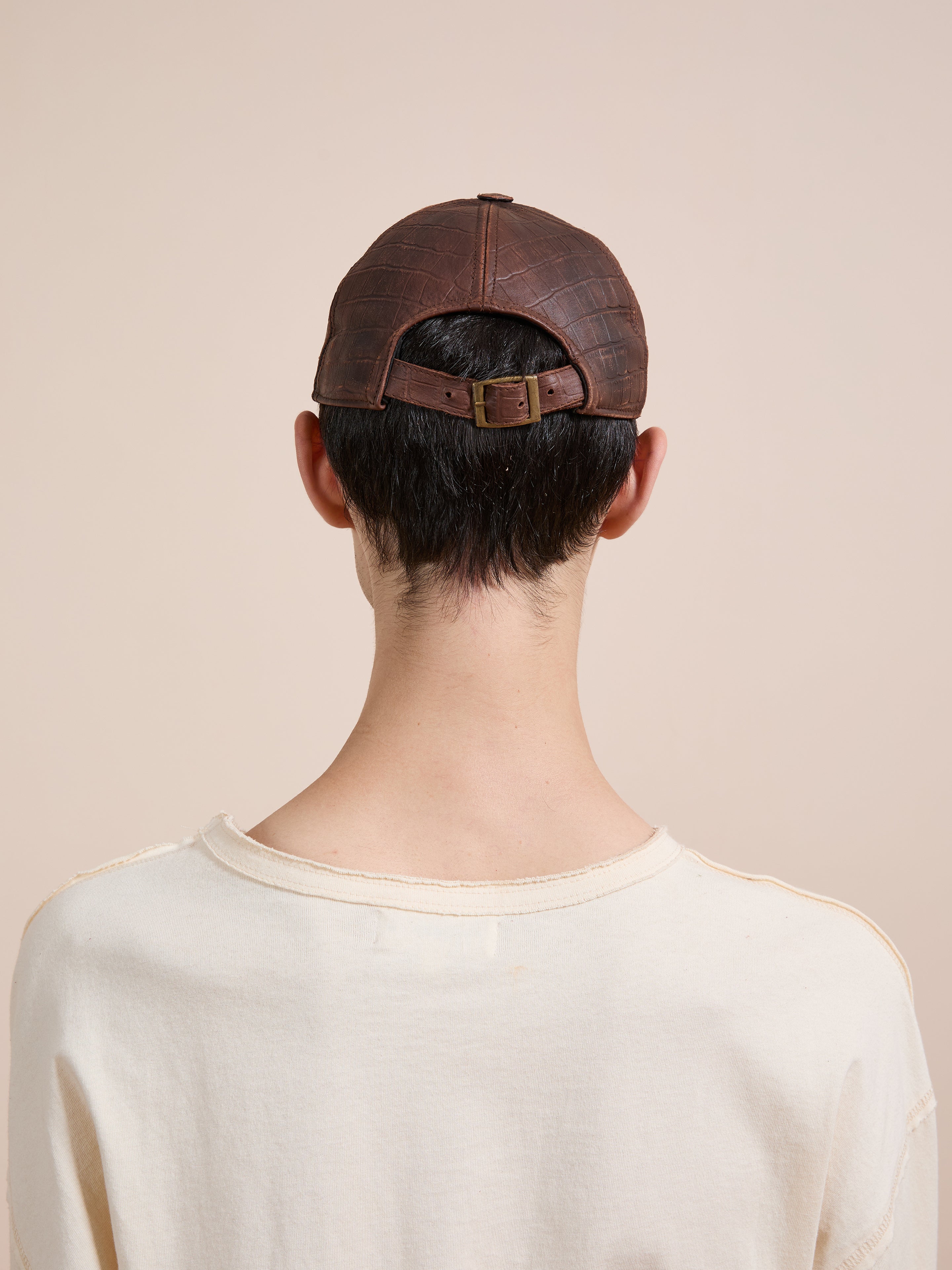 A person with short dark hair wears a cream shirt and the Found Croc Embossed Distressed Leather Cap, seen from behind against a plain beige background.