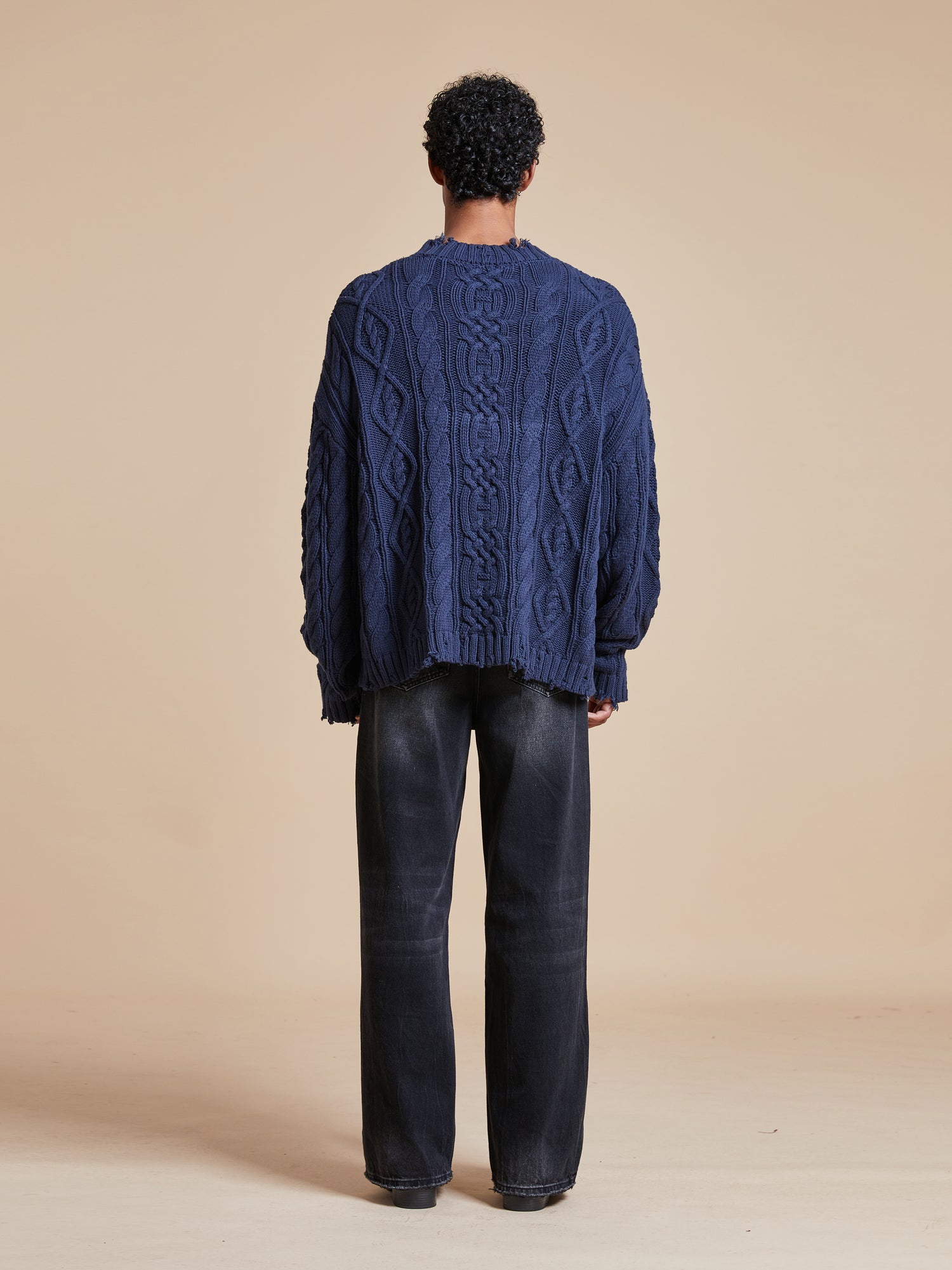 The back view of a man wearing an Astral Distressed Cable Knit Sweater made by Found.