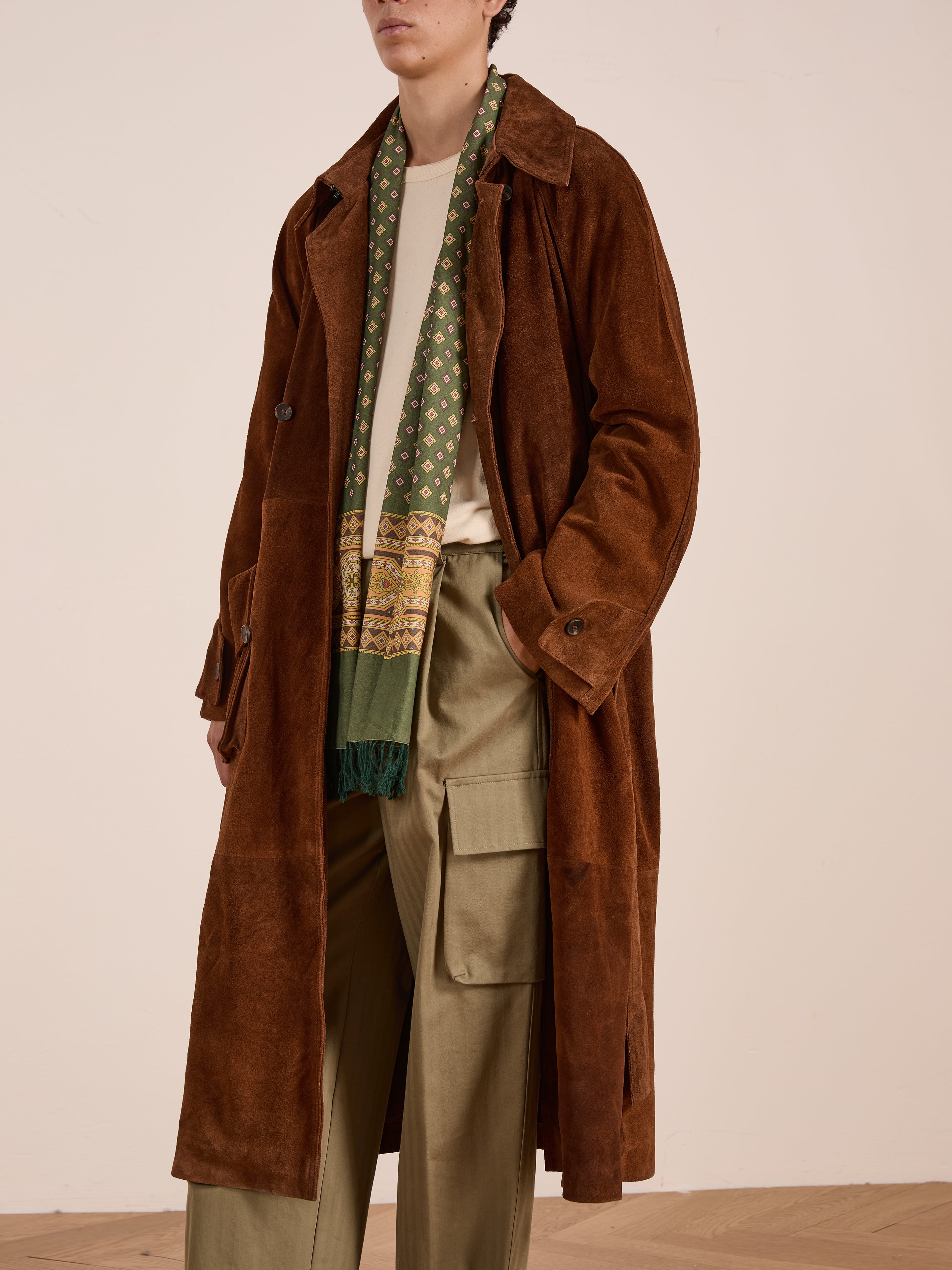 A person wearing the FOUND Suede Leather Trench Coat, a green patterned scarf, beige shirt, and olive cargo pants stands against a plain light background.