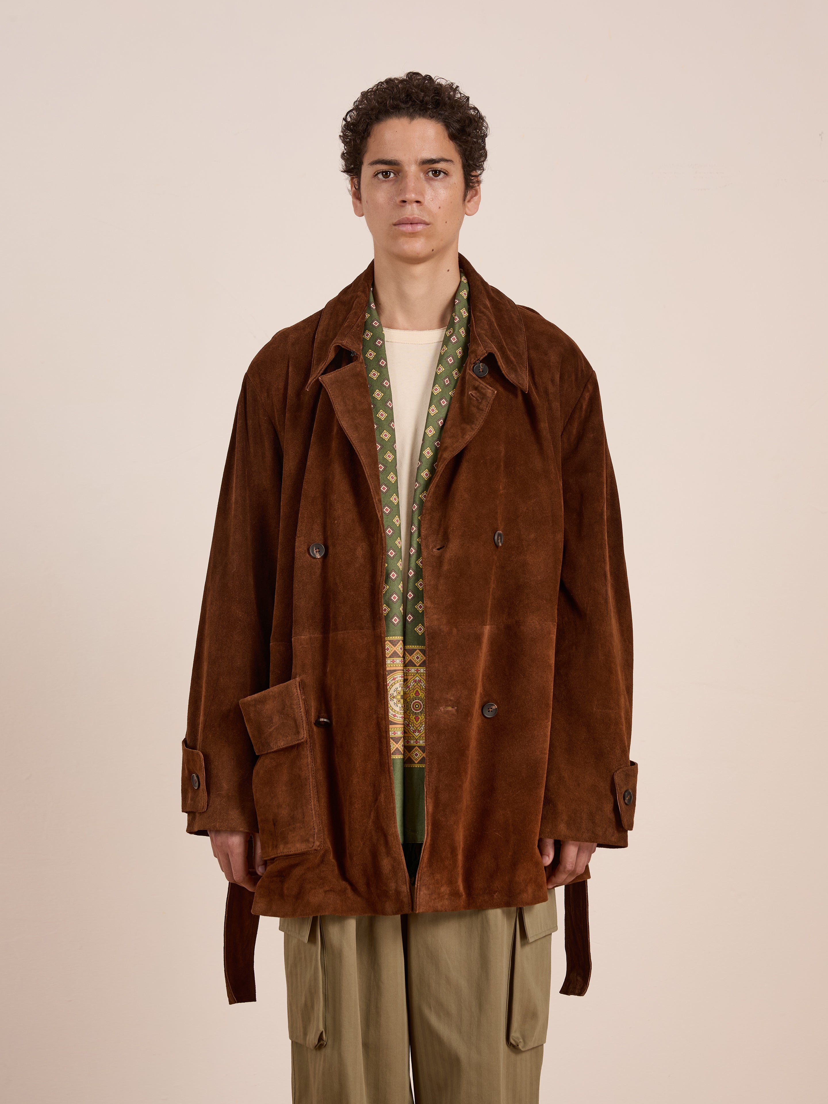 A person models the FOUND Double Breasted Suede Leather Jacket over a patterned green scarf, cream shirt, and olive cargo pants against a plain background.