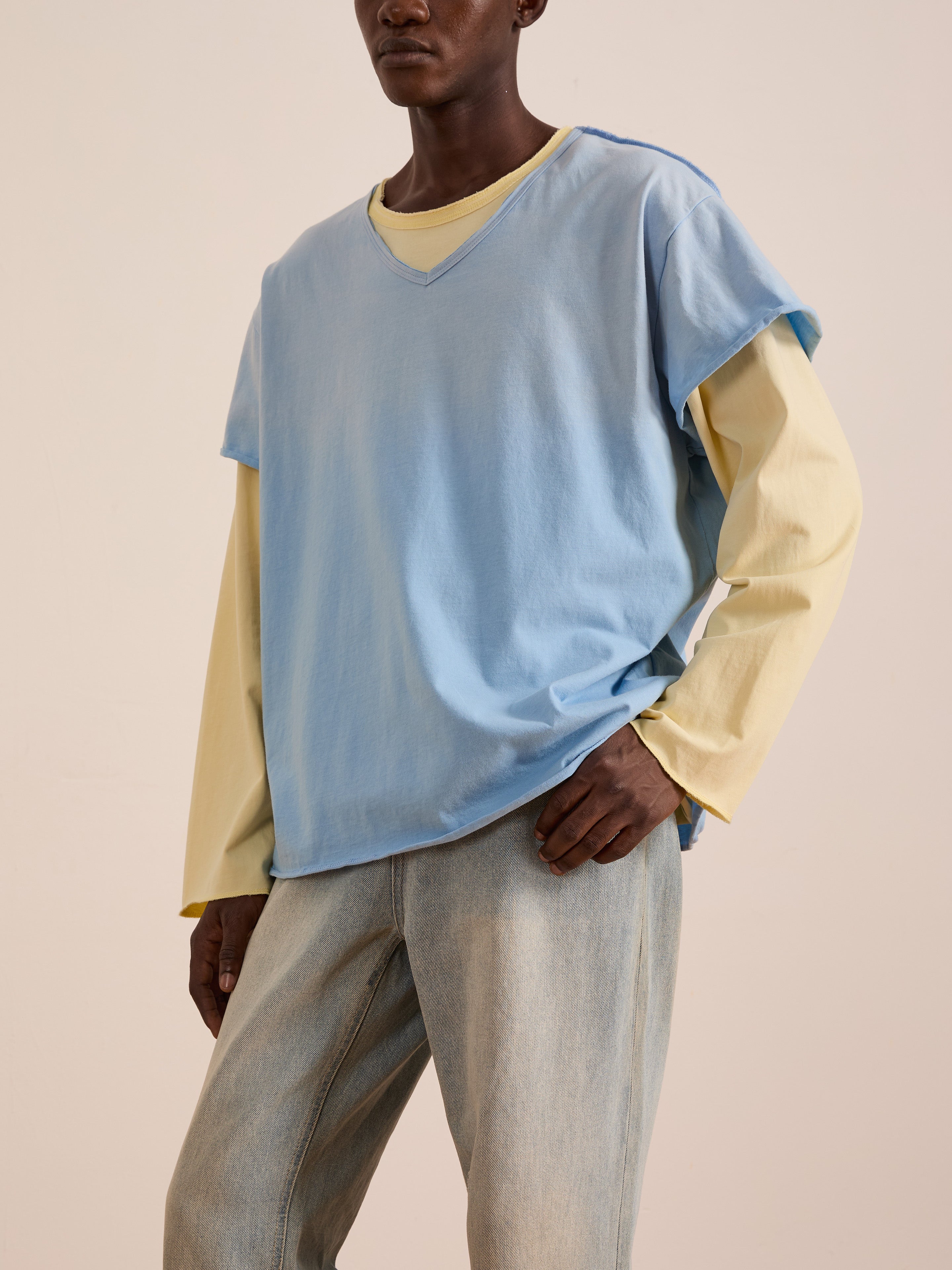 A person wears the FOUND Double Layer LS Tee—a light yellow unisex long sleeve under a loose light blue top—paired with light blue jeans, standing against a plain background.