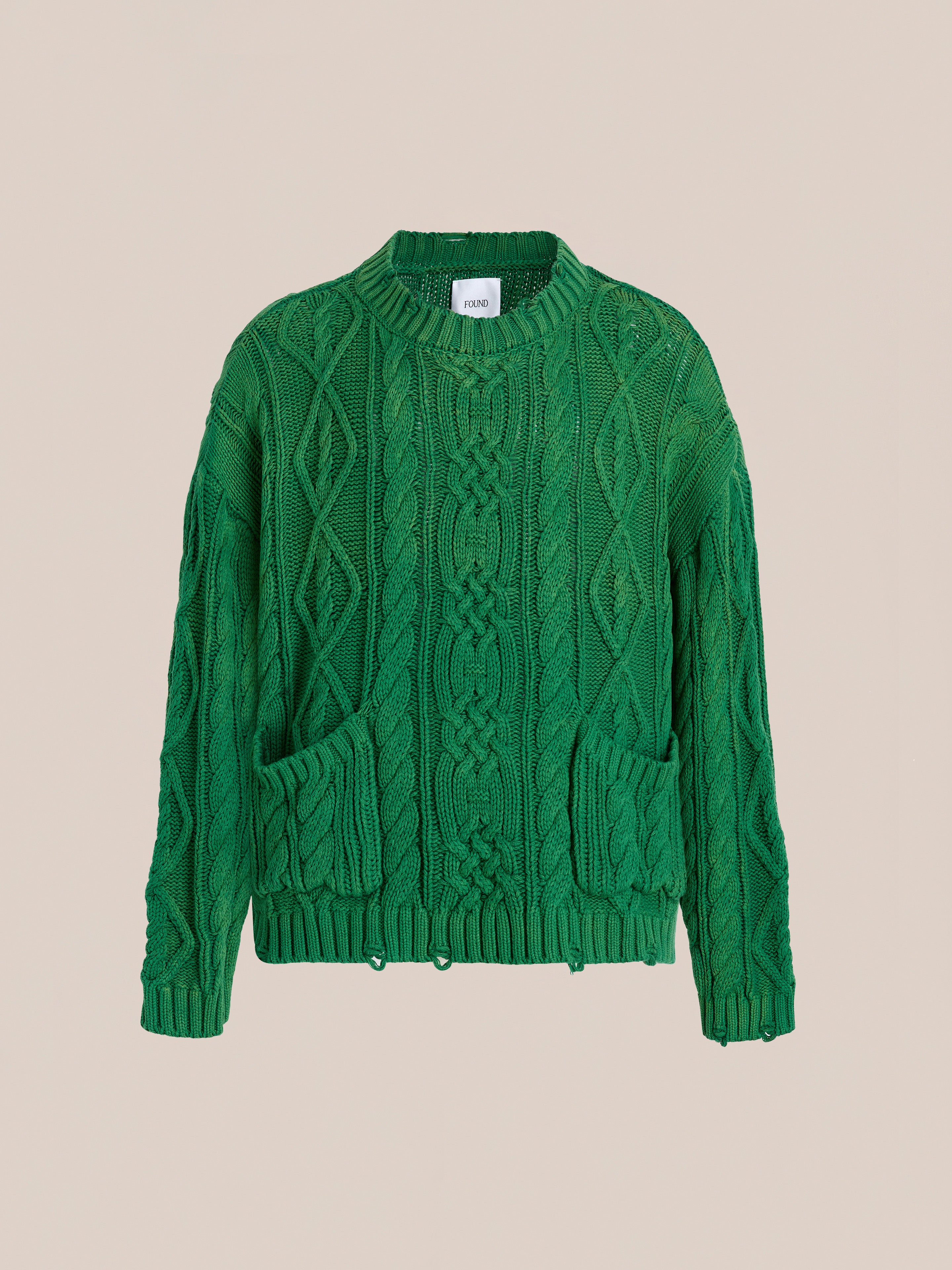 The Found Cable Knit Pullover Sweater is a green unisex chunky knit with long sleeves, crew neck, and two front pockets, displayed on a beige background—perfect for adding timeless style and comfort to your wardrobe.