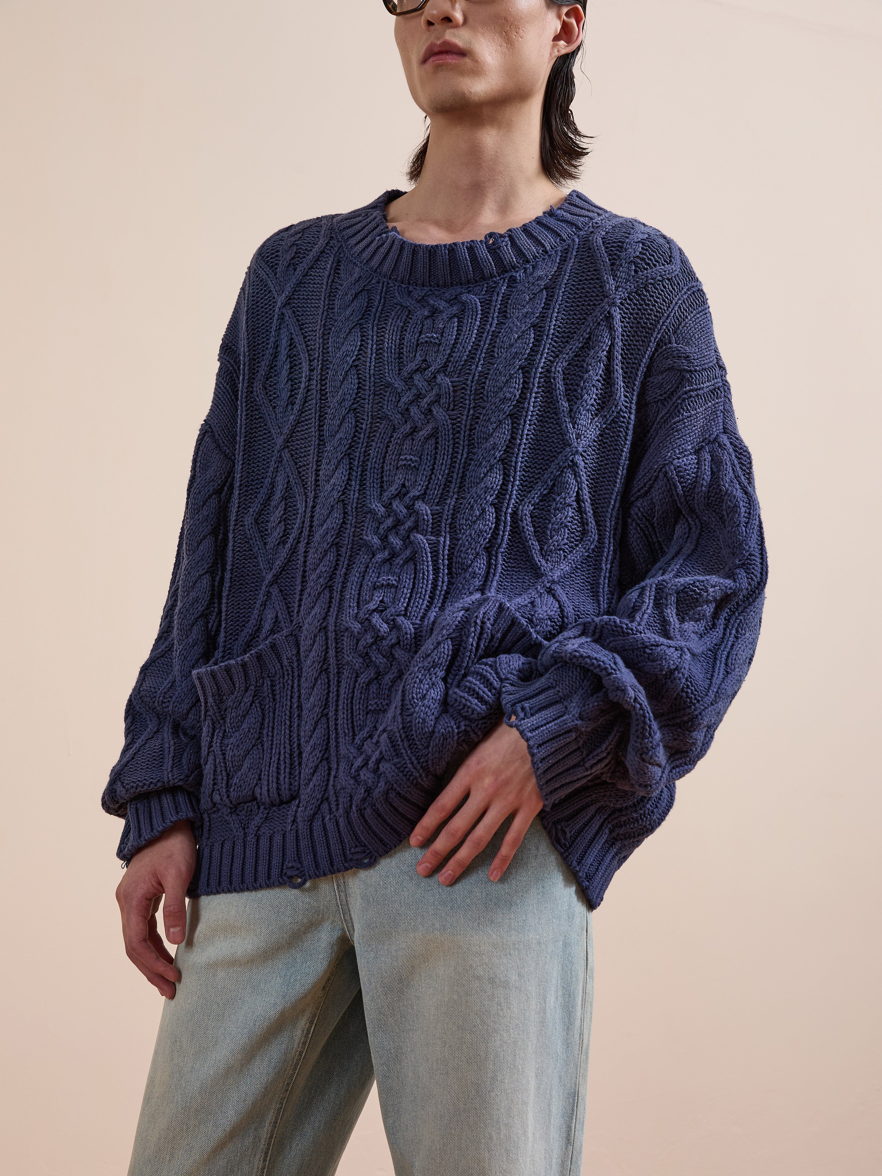 A person wears the Found Cable Knit Pullover Sweater in purple with light blue jeans, standing against a plain beige background.