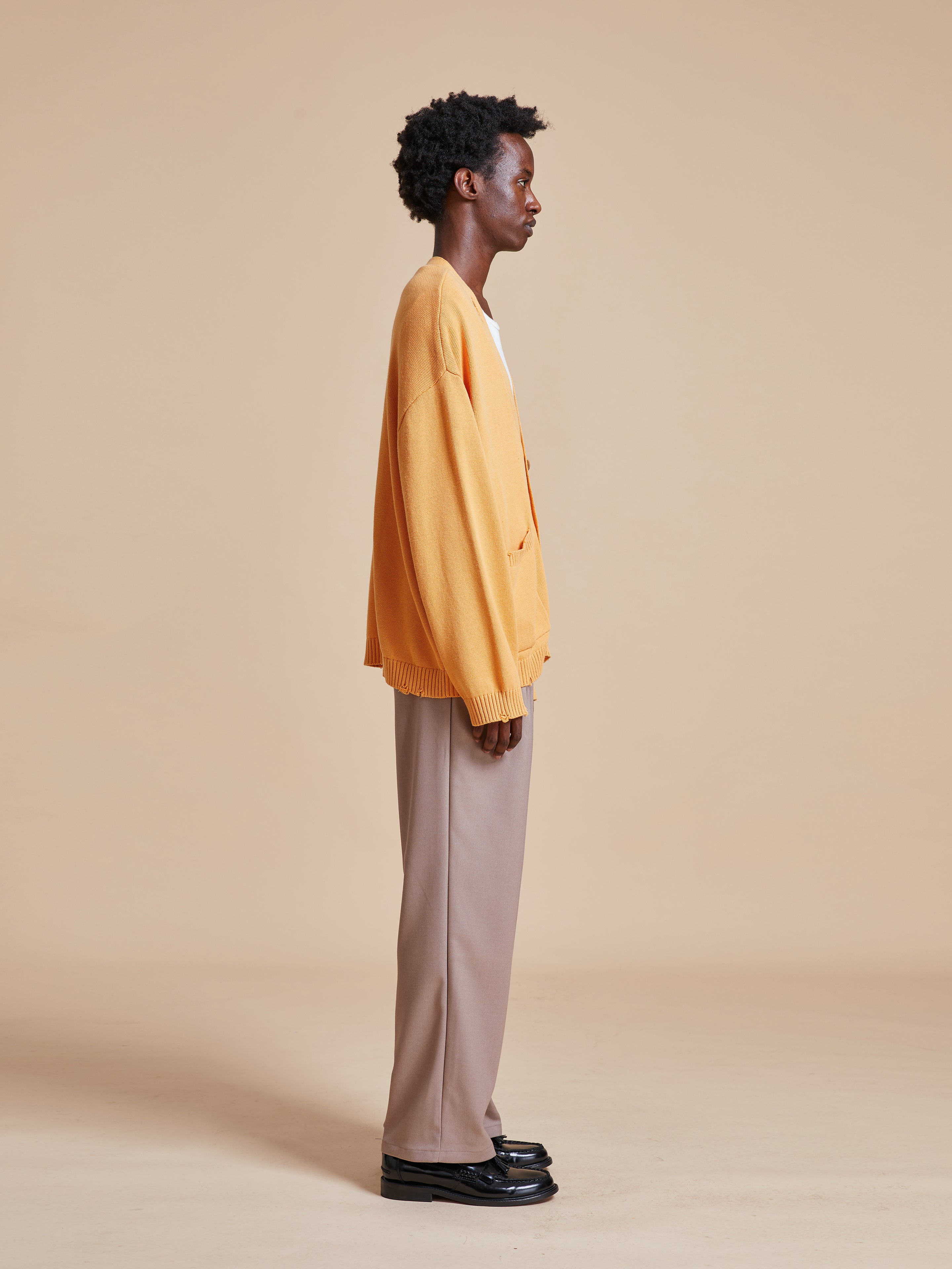 A man wearing a Found Cadmium Distressed Cardigan and tan pants.