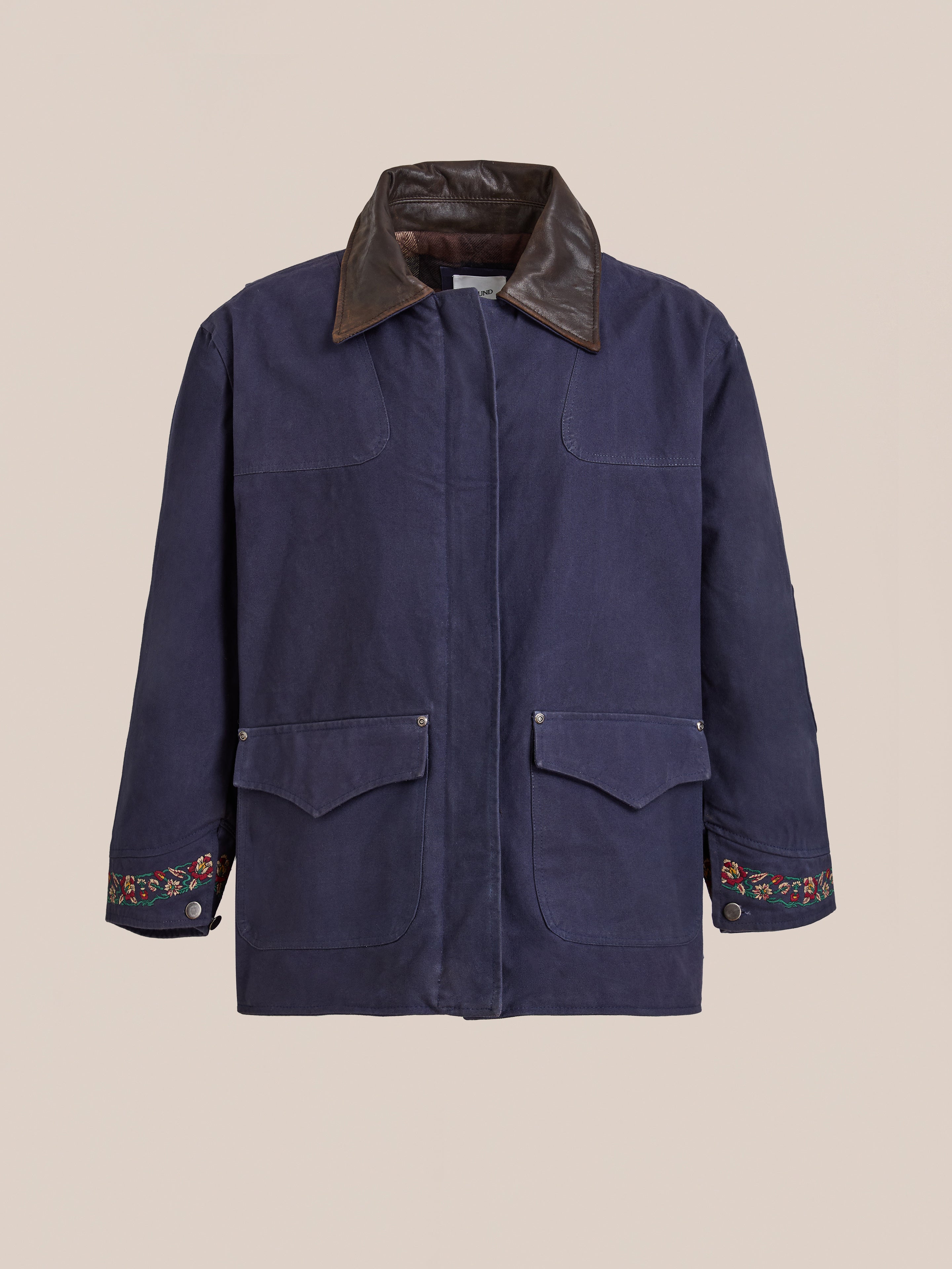 The Found Canvas Distressed Barn Jacket features a navy finish, distressed leather collar, floral-embroidered cuffs, and two front flap pockets, shown against a plain light background.
