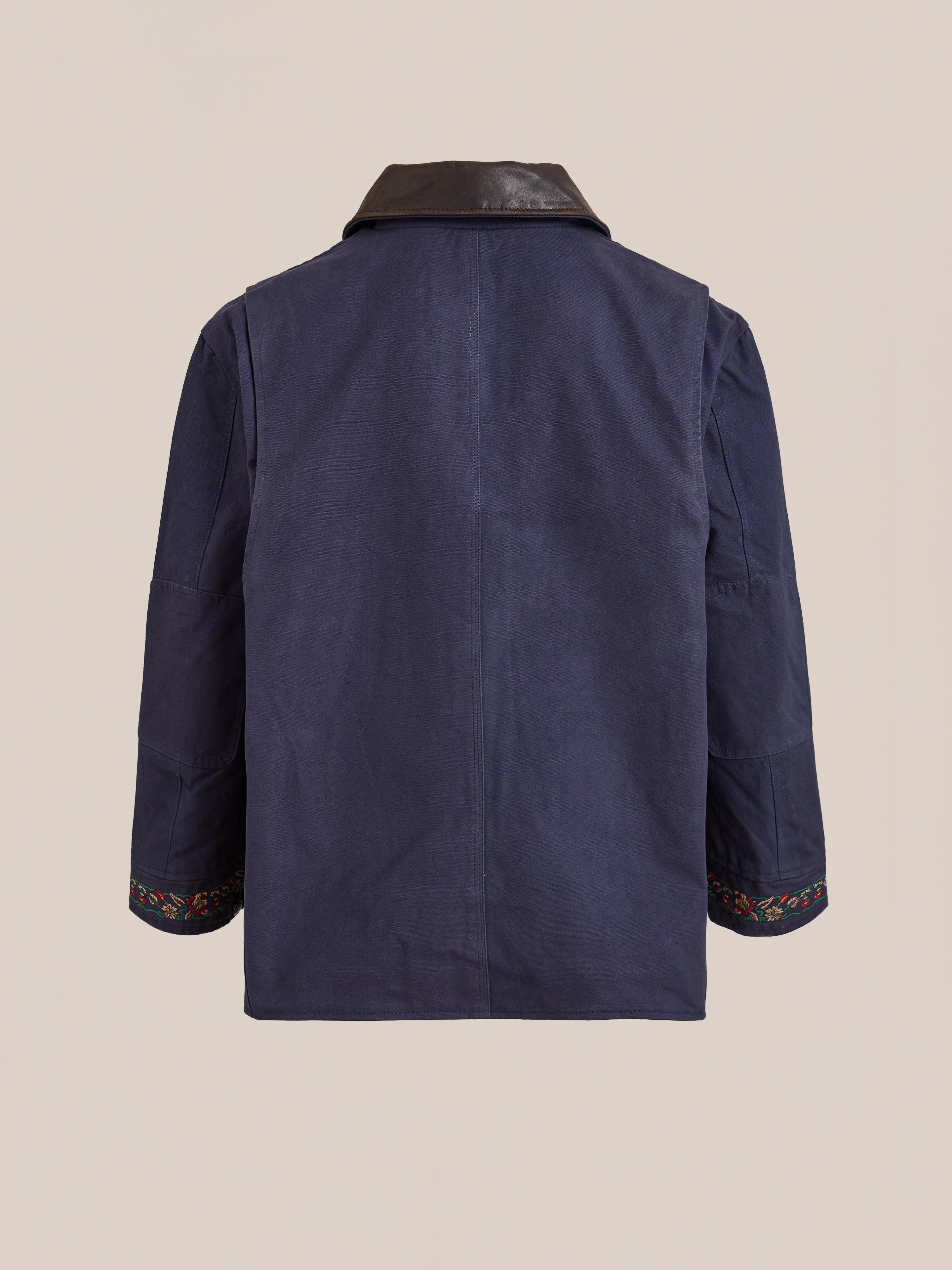 The Found Canvas Distressed Barn Jacket features a navy finish, relaxed unisex fit, distressed leather collar, long sleeves, and colorful embroidery on the sleeve cuffs, shown from the back.