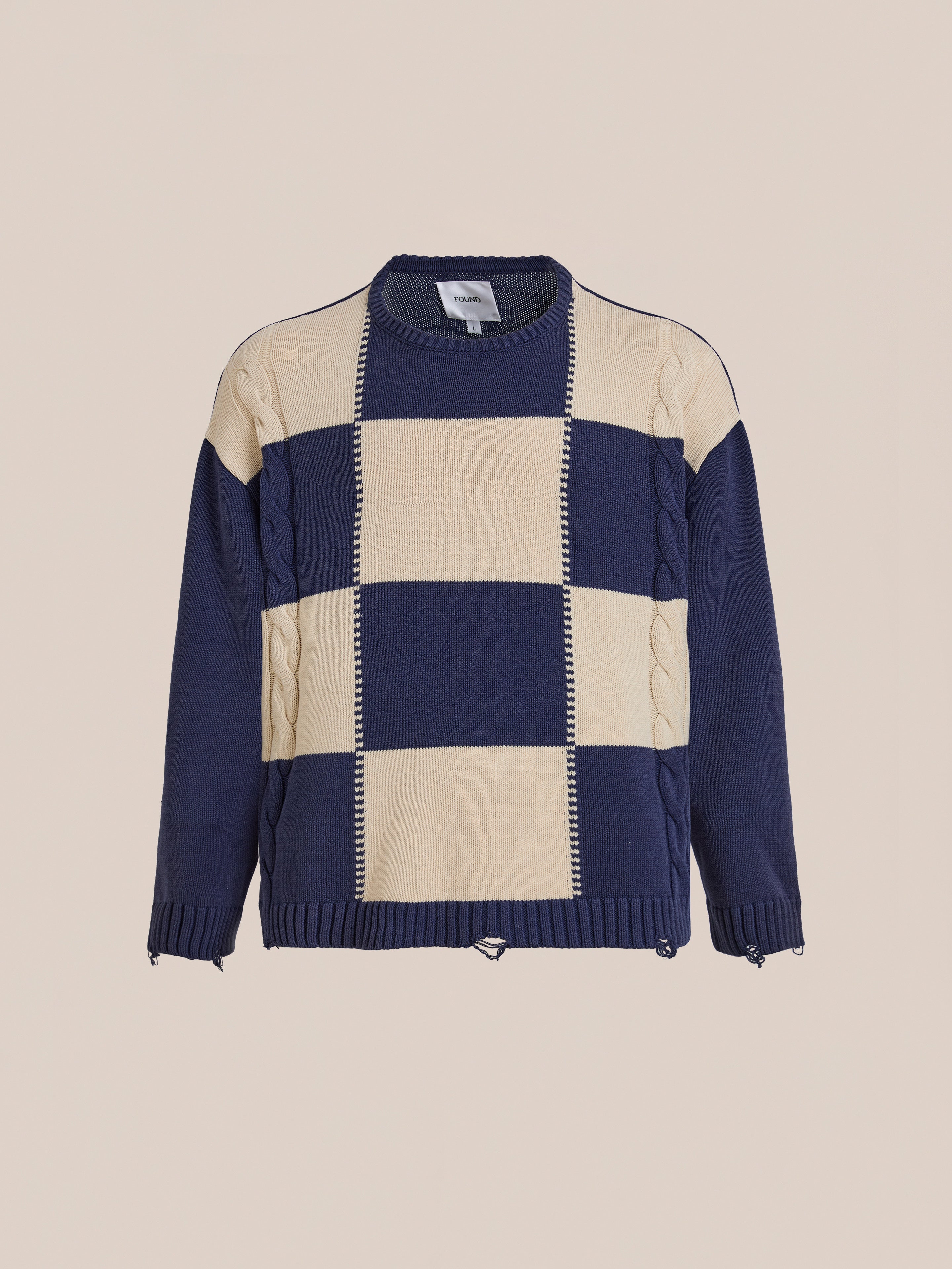 The Found Checkered Fisherman Sweater has a relaxed unisex fit, navy blue and beige checkered pattern, ribbed cuffs and hem, and visible cable knit details on the sleeves.