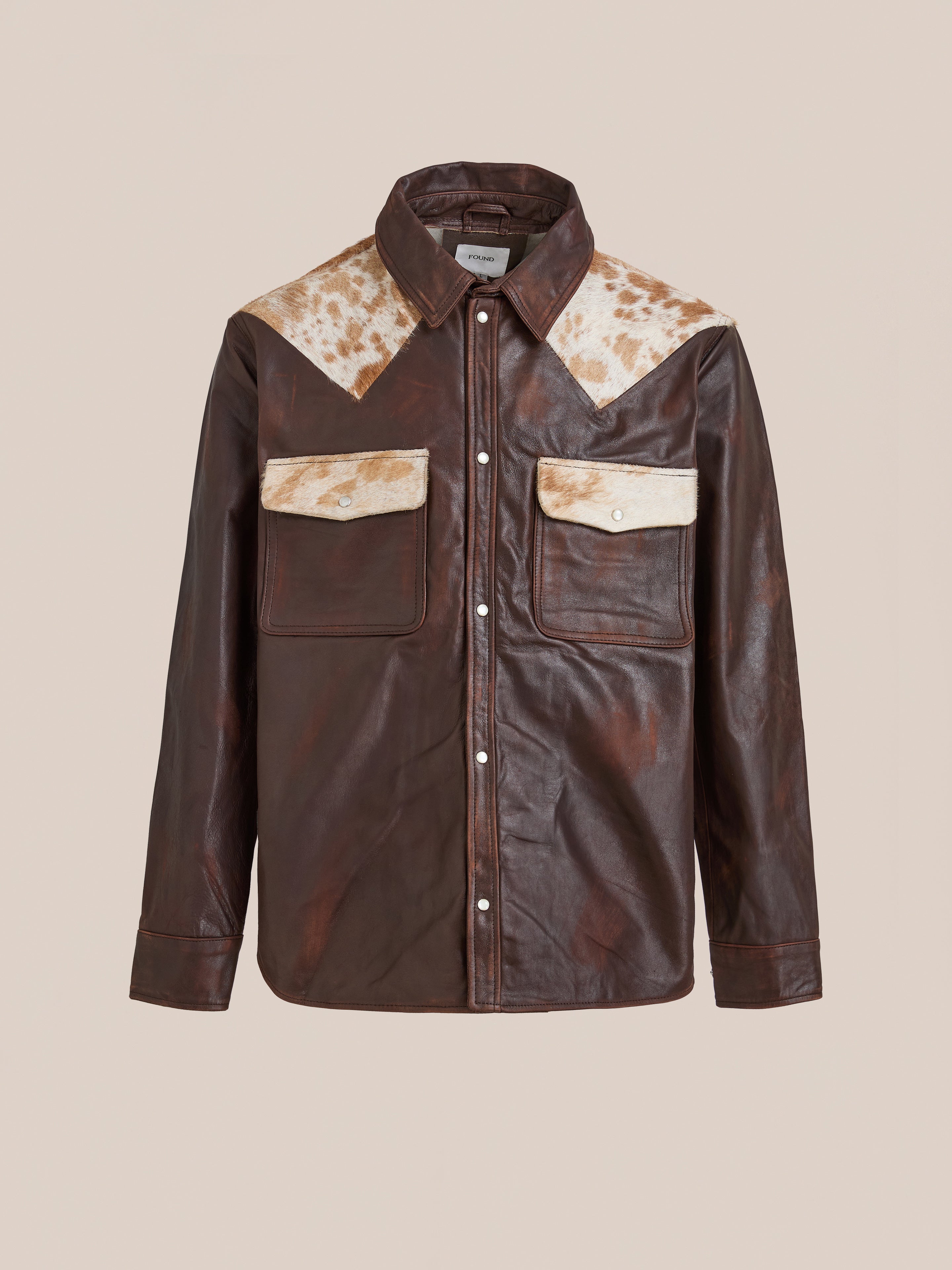 The FOUND Distressed Leather Cowhide Contrast Western Shirt is crafted from genuine brown leather with beige cowhide accents, snap buttons, and two front flap pockets for an authentic Western style.