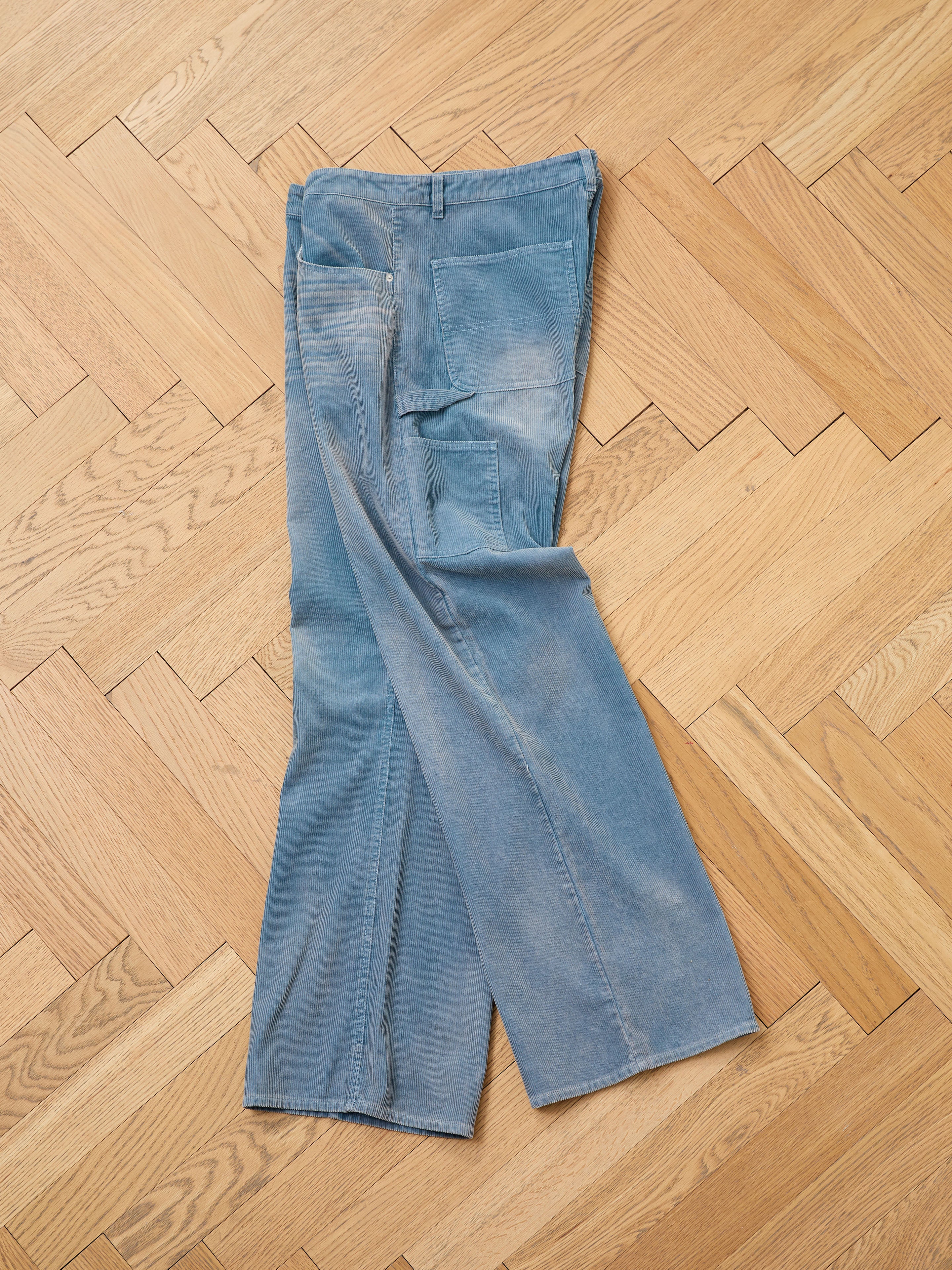 FOUND Corduroy Flare Work Pants are shown laid flat and crossed at the ankles on a wooden herringbone-pattern floor, featuring visible wear, fading, and a relaxed fit.