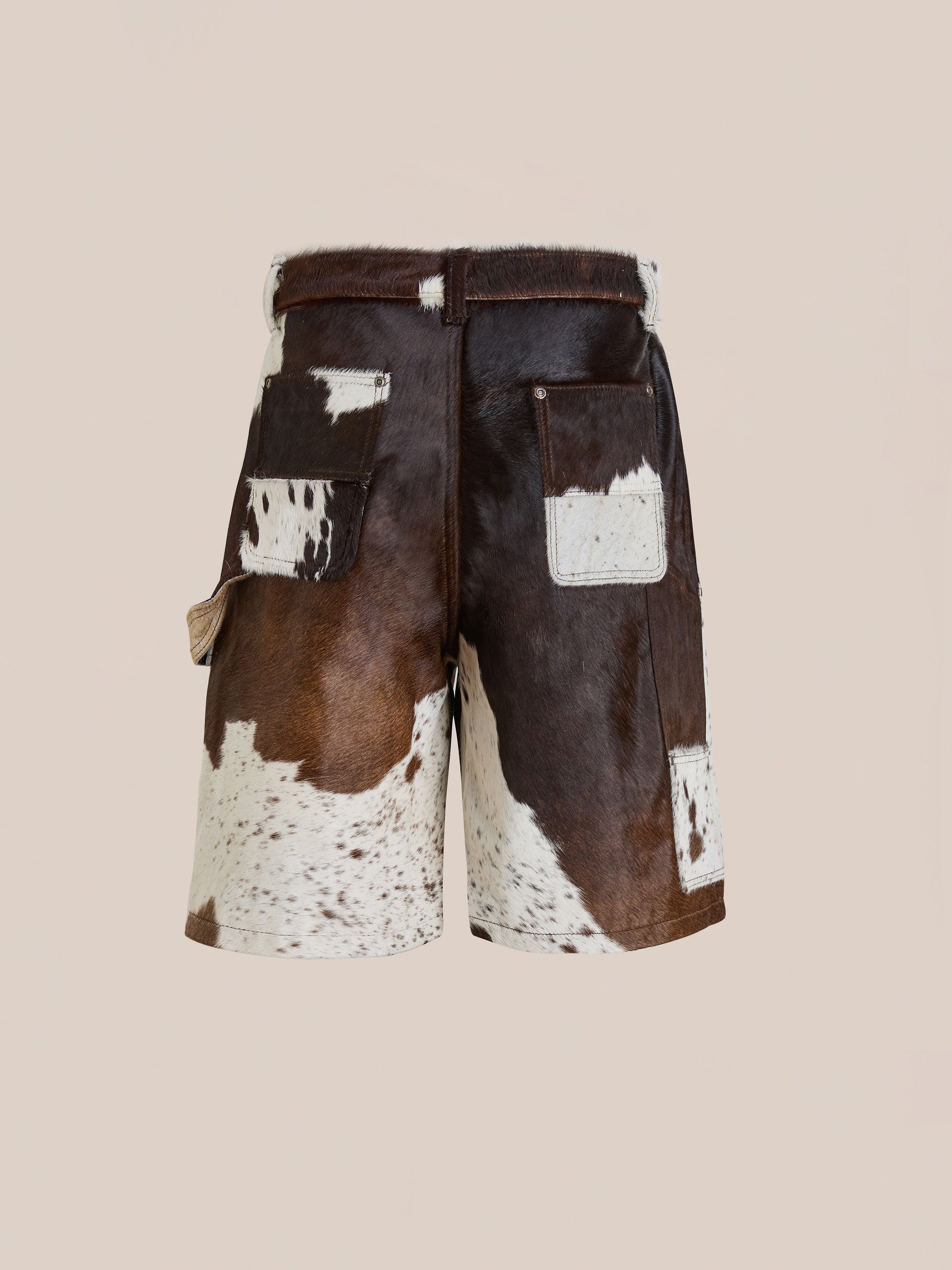 Found’s Cowhide Prairie Carpenter Shorts are unisex, relaxed fit shorts crafted from genuine brown and white cowhide leather with patchwork details and visible texture, shown on a plain beige background.
