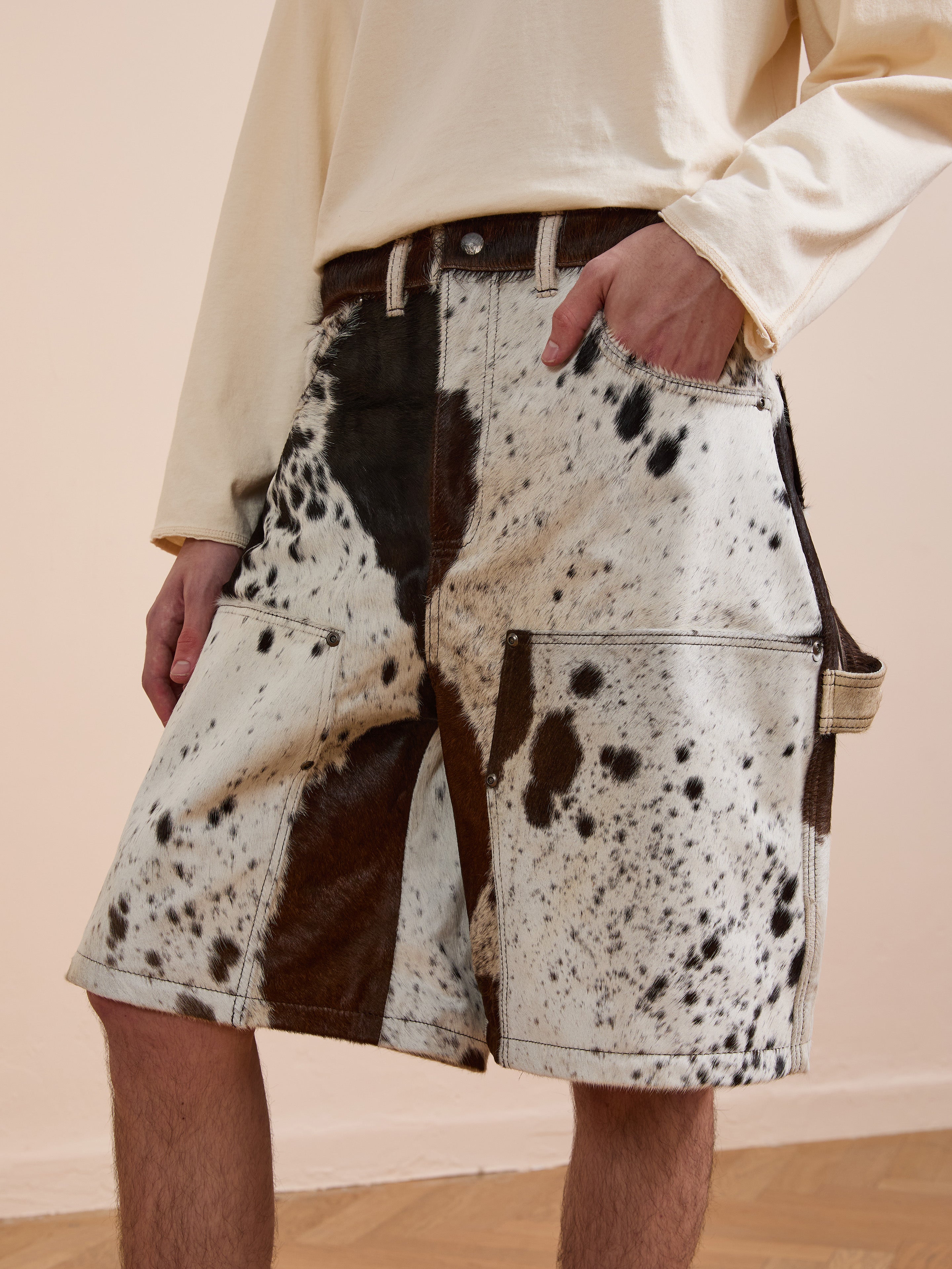 Indoors, a person in a light long-sleeve shirt wears Found's Cowhide Prairie Carpenter Shorts with a relaxed fit, standing with one hand in their pocket.