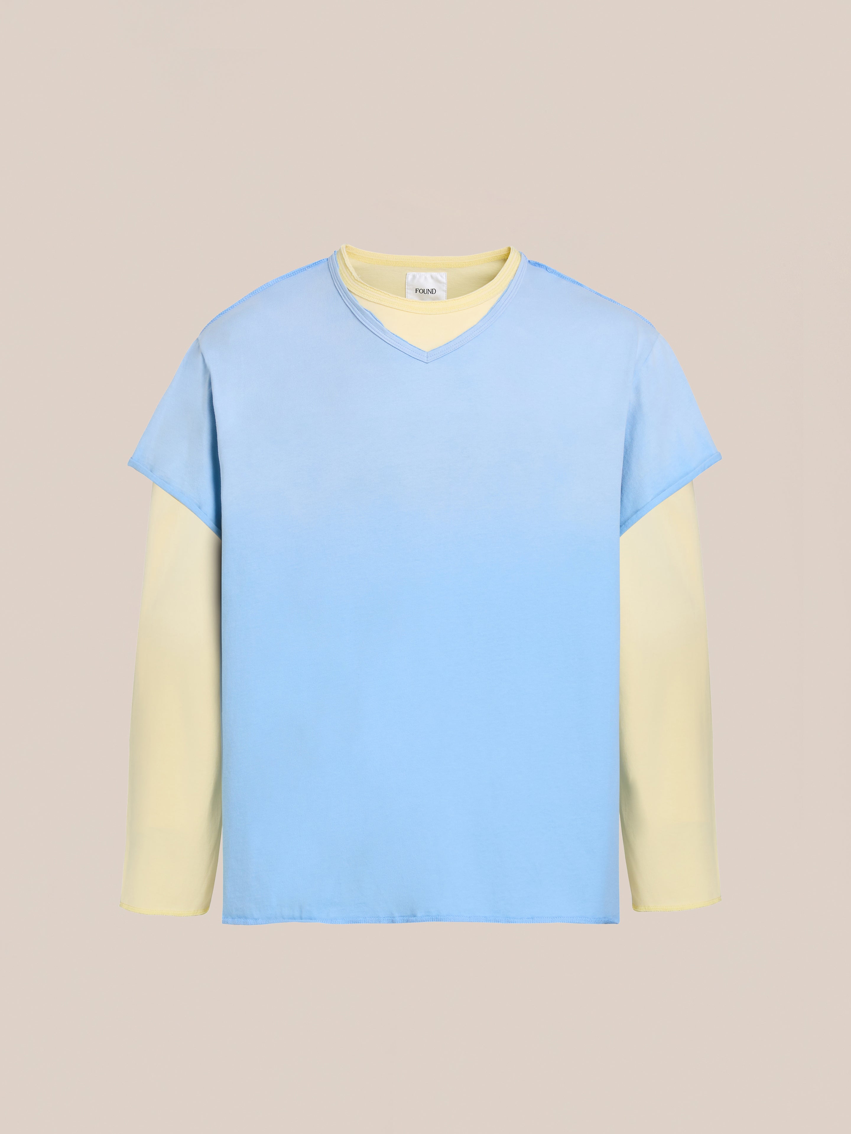 The FOUND Double Layer LS Tee is a unisex long sleeve shirt with cream sleeves beneath a light blue sunfade wash V-neck, shown on a plain beige background.