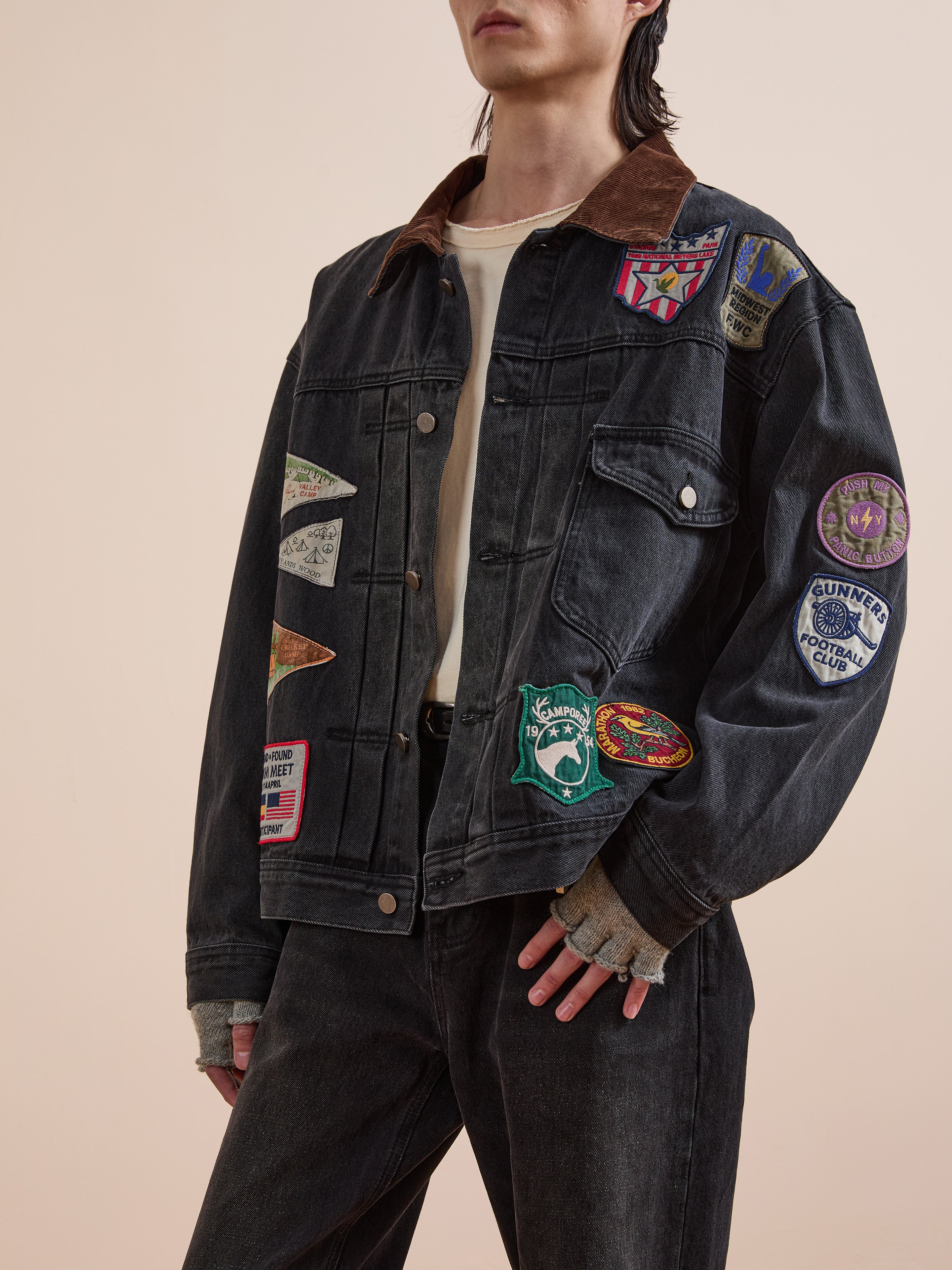 Model wears the FOUND Denim Patchwork Jacket, featuring Americana patches over a white shirt and dark jeans, standing against a plain background.
