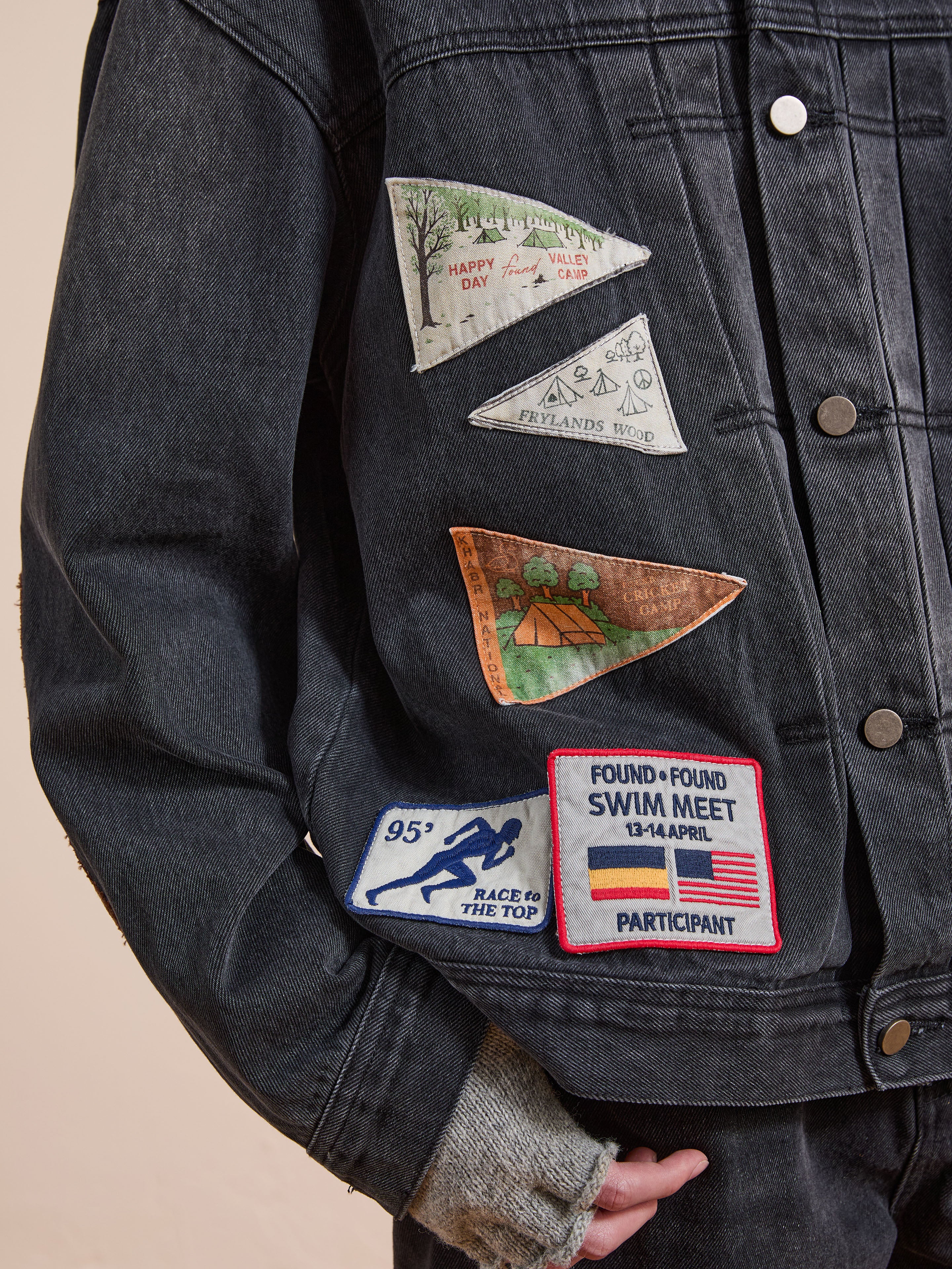 A person wears the FOUND Denim Patchwork Jacket, a vintage-inspired piece with a corduroy collar and four vibrant Americana patches in different designs and text.