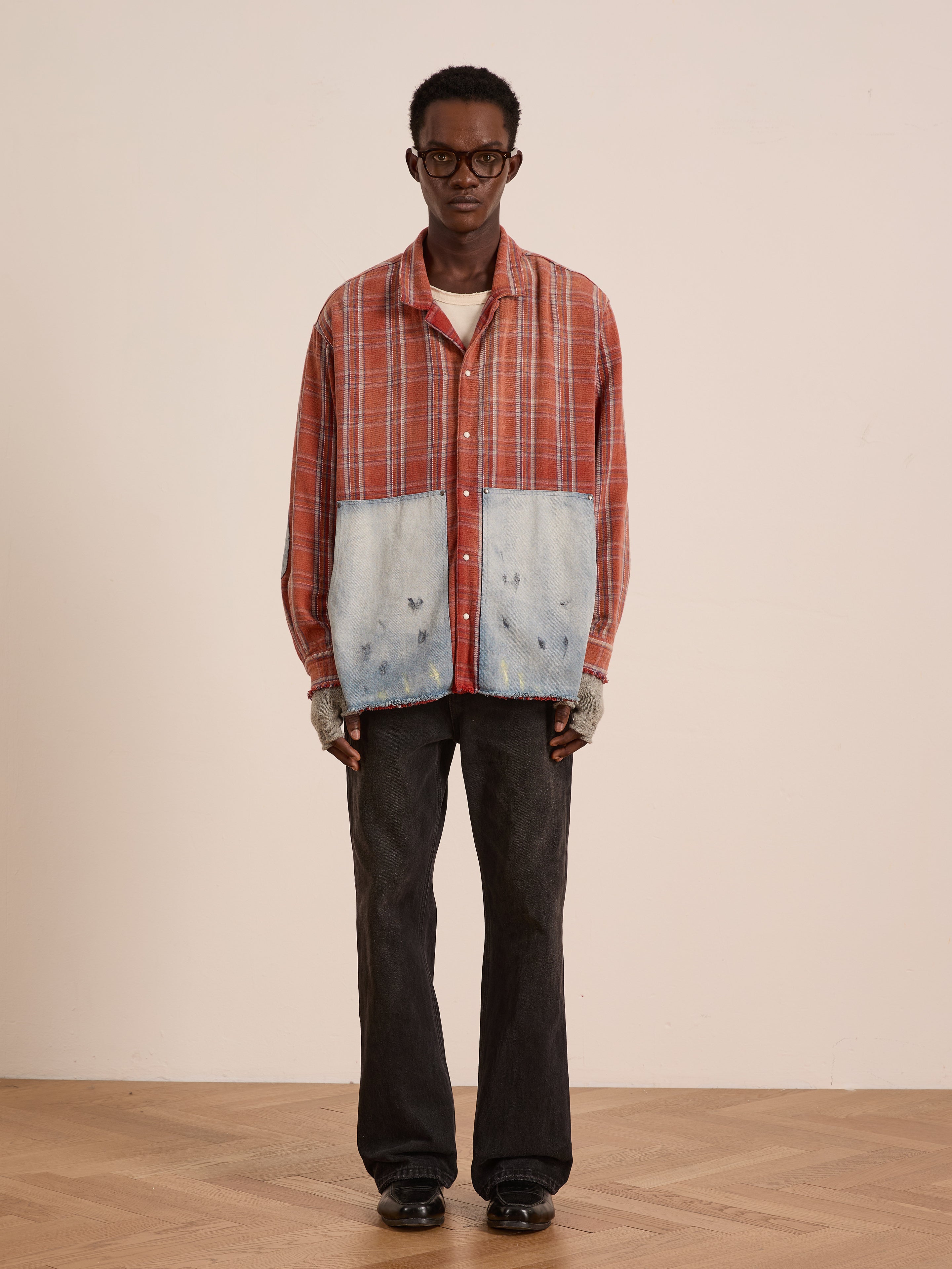 Indoors, a person wears the FOUND Plaid Denim Shirt with oversized carpenter pockets, paired with black pants, black shoes, gray fingerless gloves, and glasses.