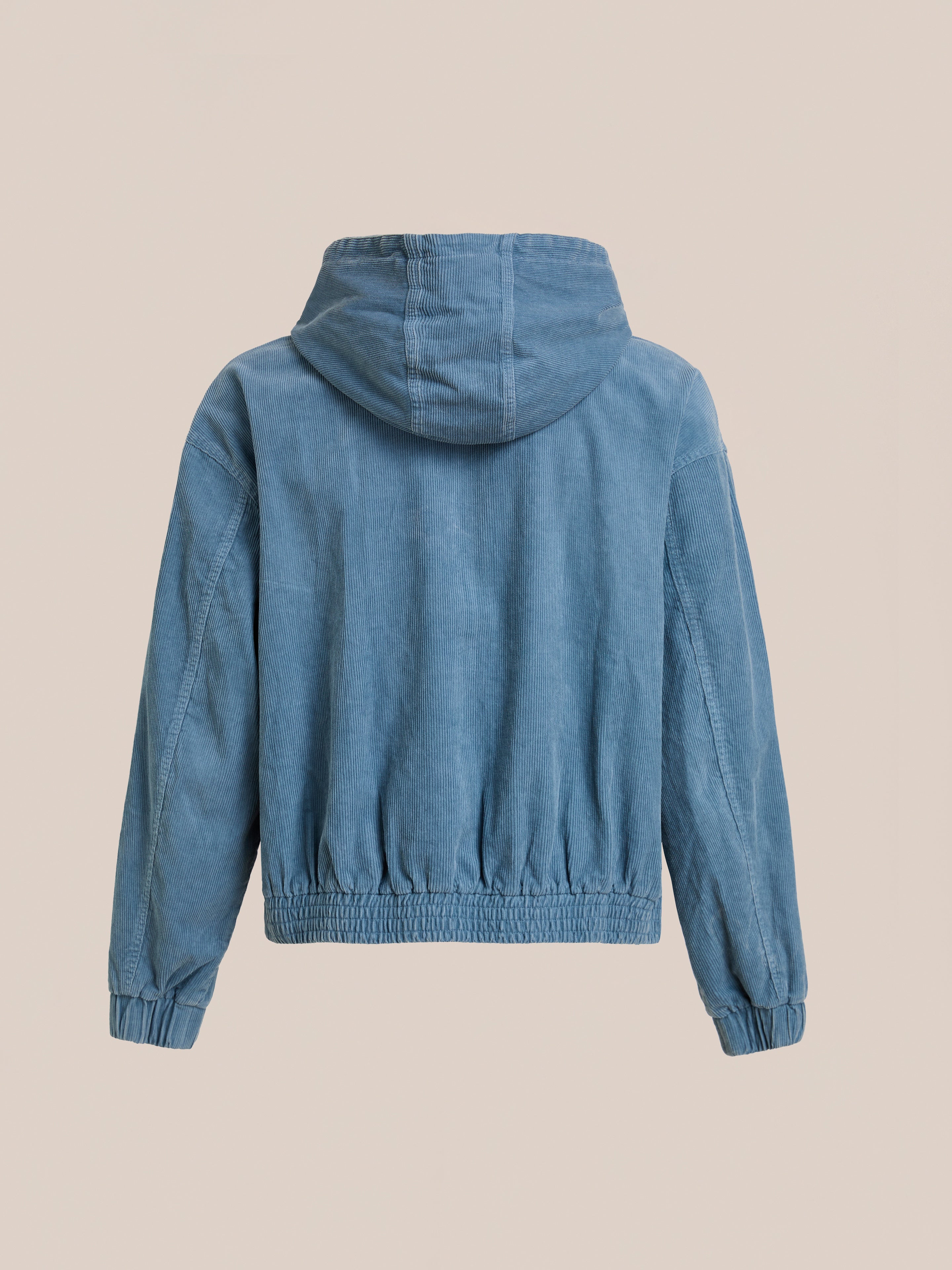 The FOUND Corduroy Zip Up Hoodie is displayed from the back, showcasing its faded blue color, long sleeves, elastic cuffs and hem, all set against a plain beige background.