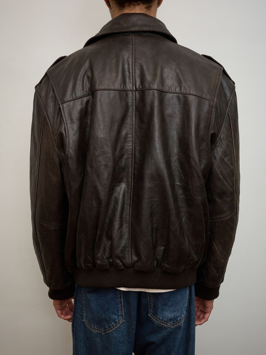 A person wearing the FOUND Distressed Leather Flight Jacket in dark brown with blue jeans, shown from the back against a plain light-colored background.