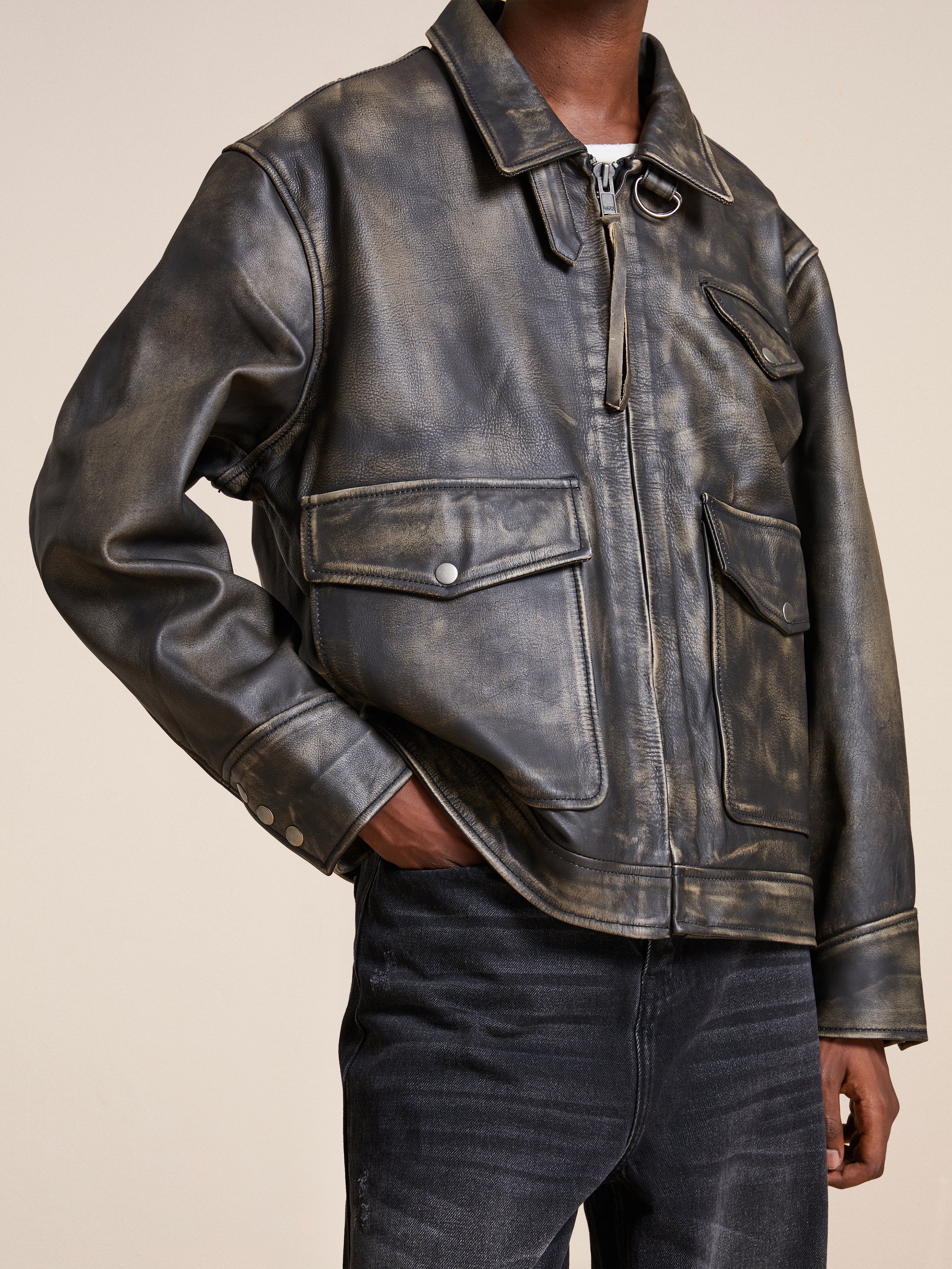 A person wears the "Distressed Leather Pocket Jacket" by Found, a cowhide leather piece with an antique feel, large pockets, light metal buttons, and a collar, paired with dark jeans.
