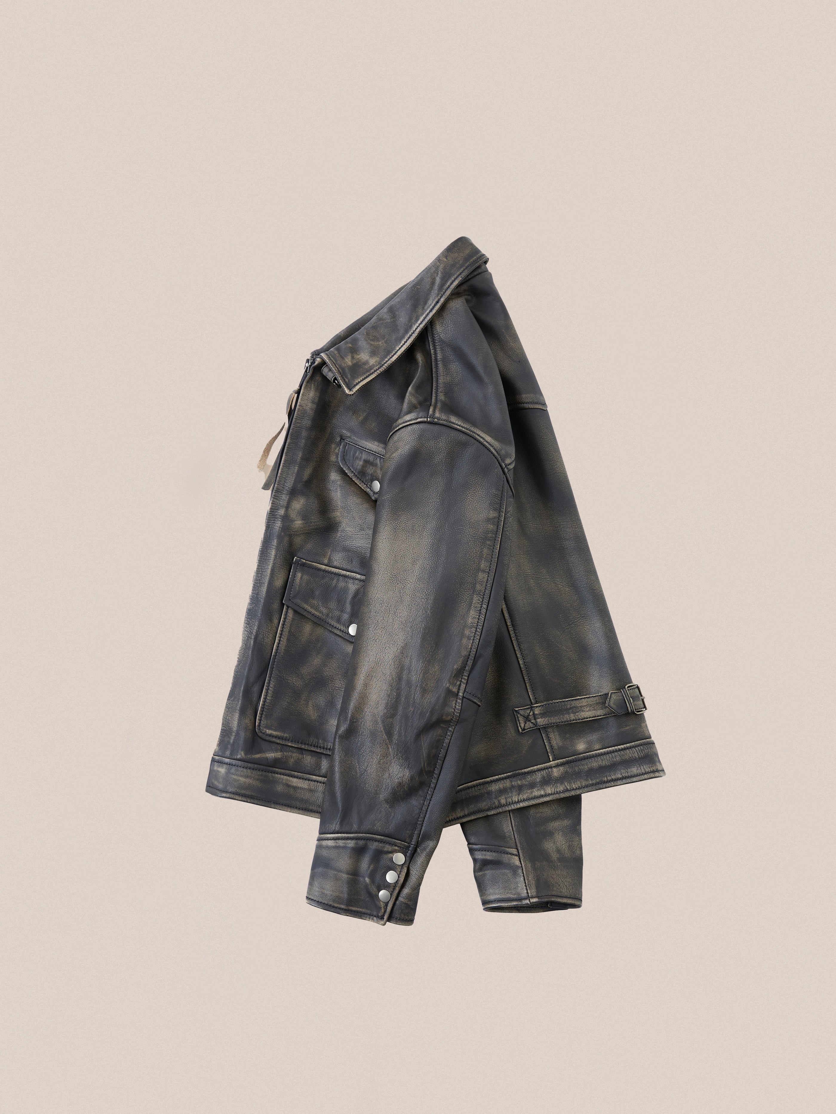 The Distressed Leather Pocket Jacket by Found, made from vintage-style black distressed cowhide leather, hangs on a beige background, exuding an antique feel.