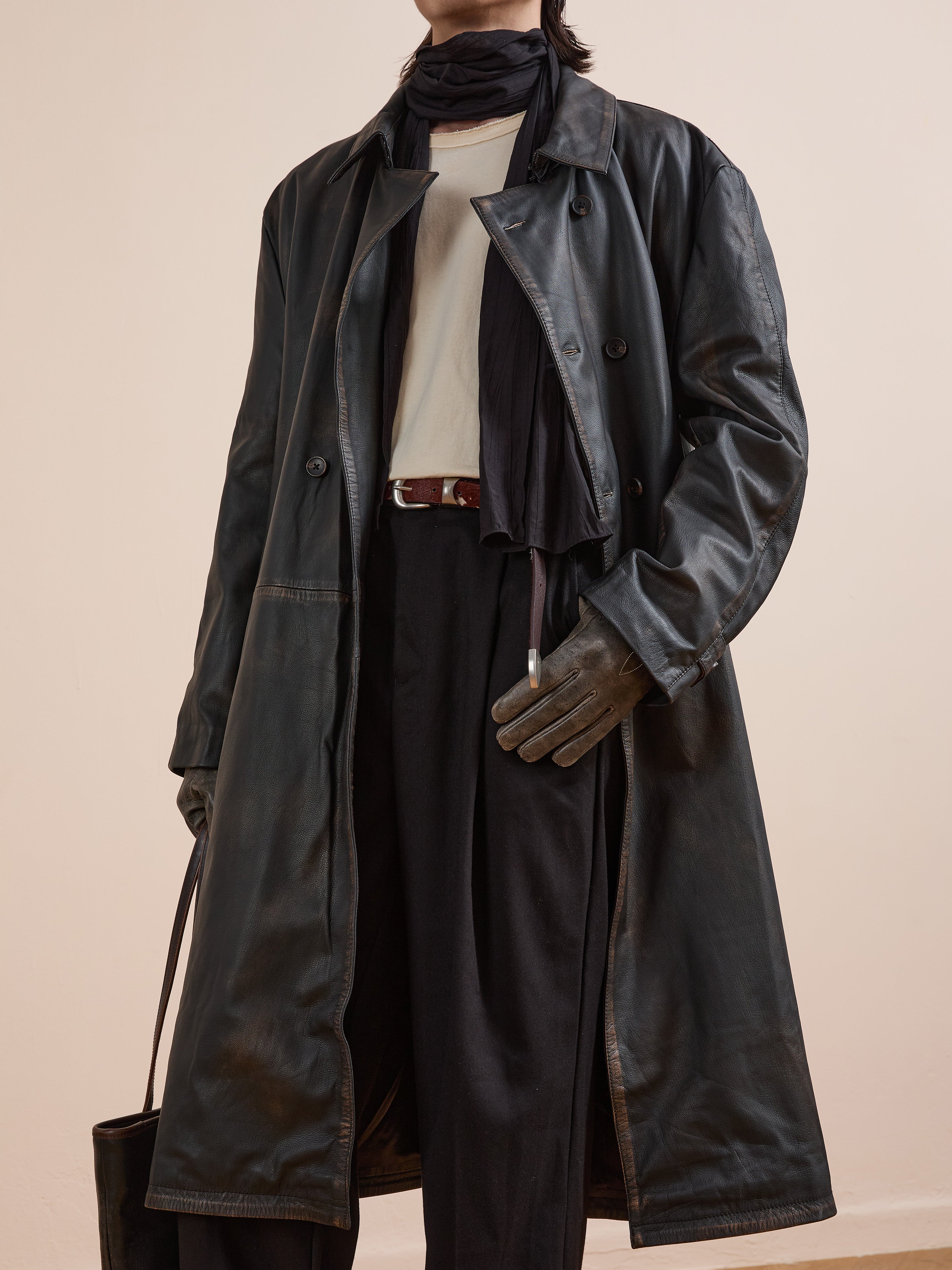 Person wearing the FOUND Distressed Leather Trench Coat, black gloves, black scarf, white shirt, black pants, and holding a black bag. Face is partially out of frame.