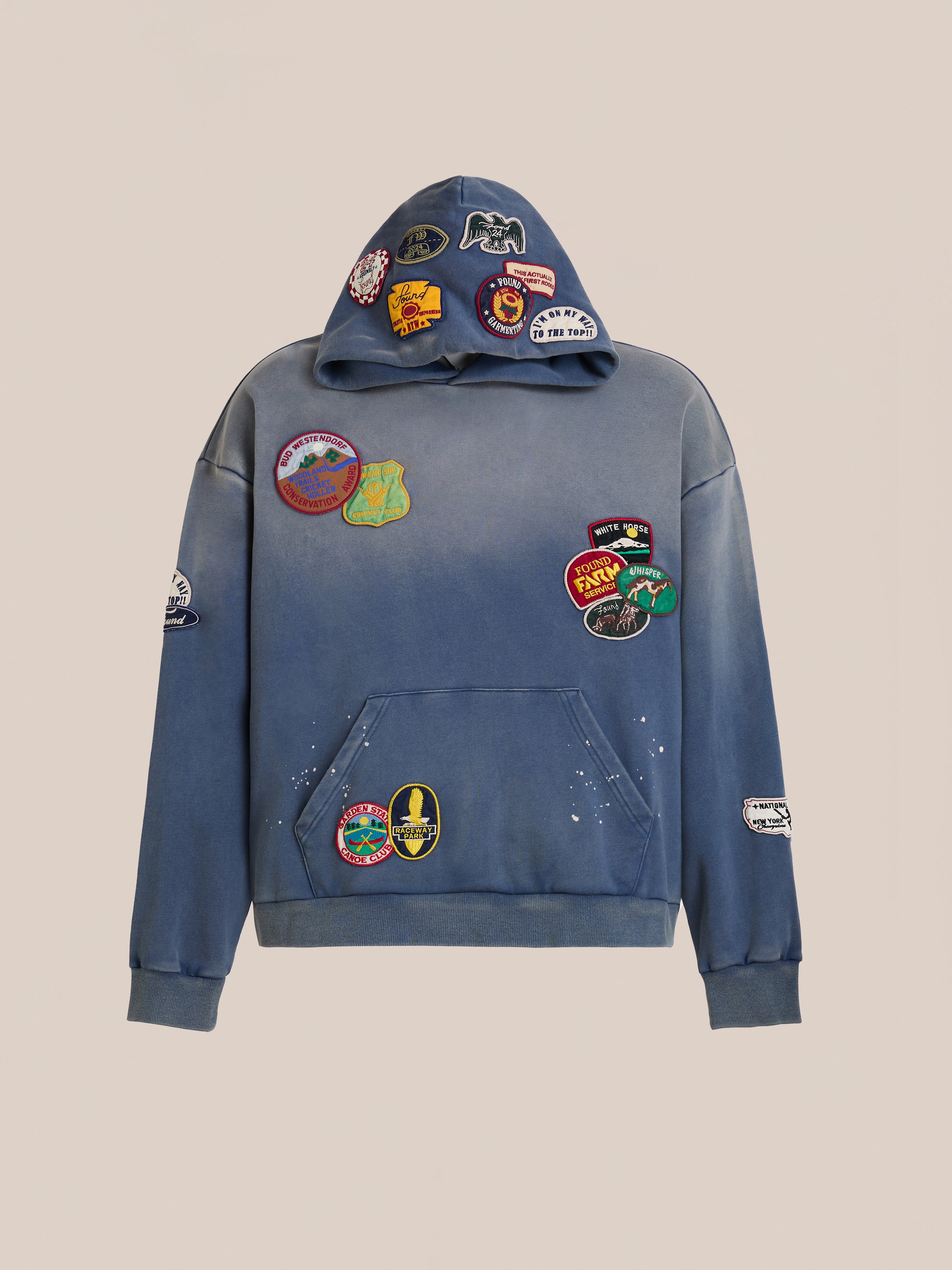 The FOUND Distressed Patch Hoodie is a blue French Terry cotton hoodie with a front pocket and vibrant embroidered patches on the hood, sleeves, and chest.