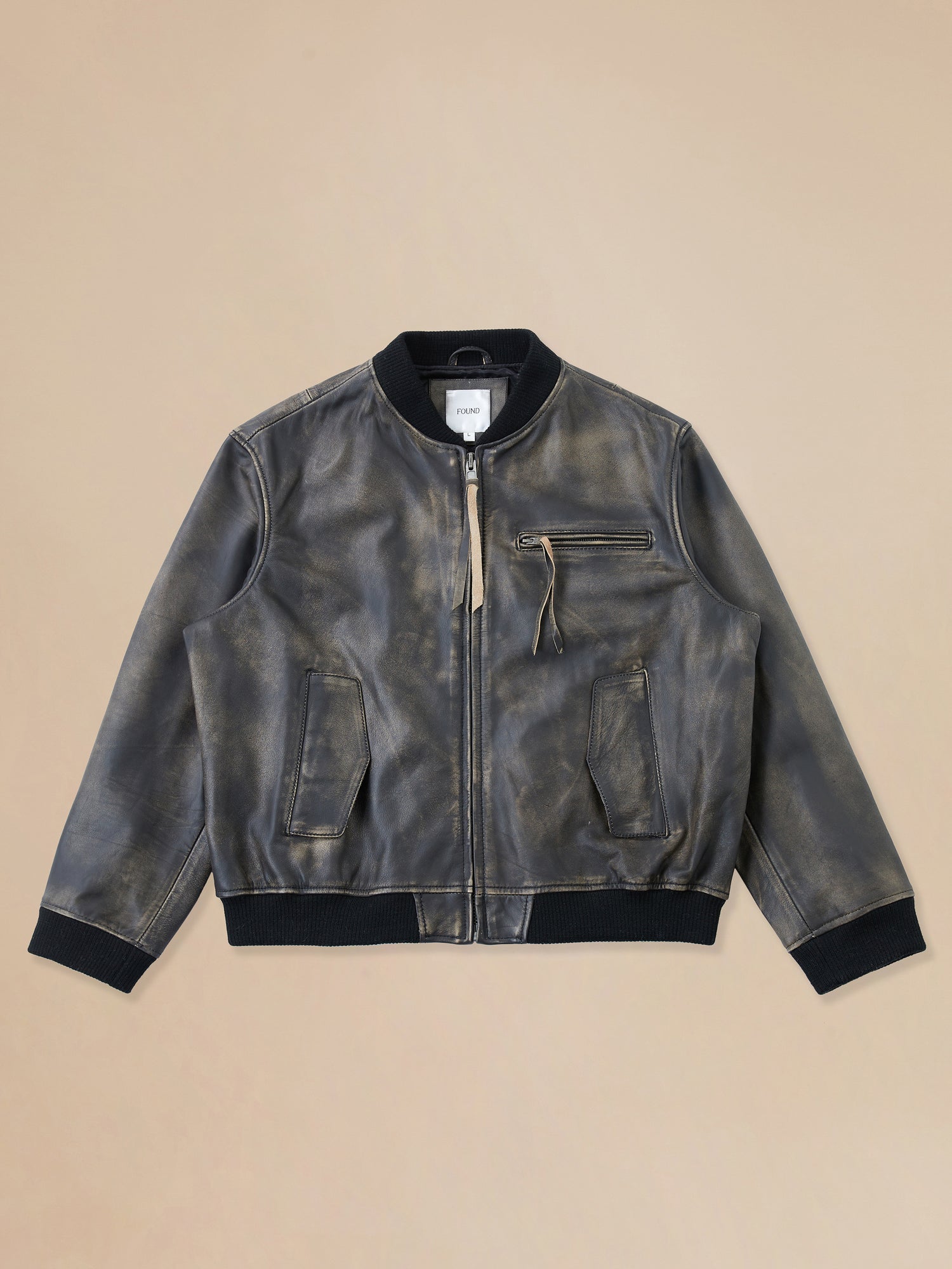 A Distressed Pavement Leather Bomber Jacket by Found on a beige background.