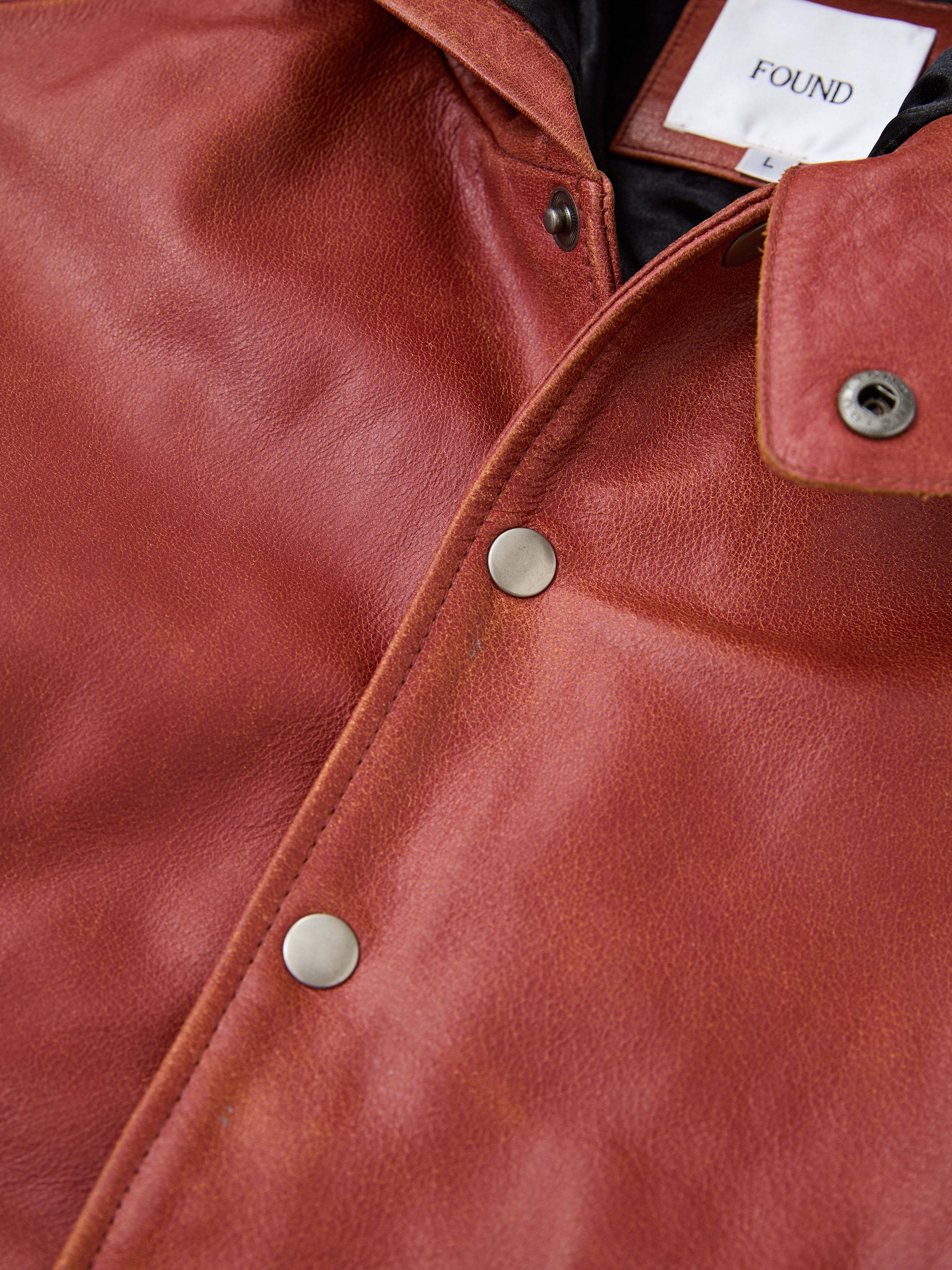 Close-up of the Distressed Leather Pocket Hoodie by FOUND, featuring genuine cowhide leather, metallic snap buttons, and a visible white tag labeled "FOUND.