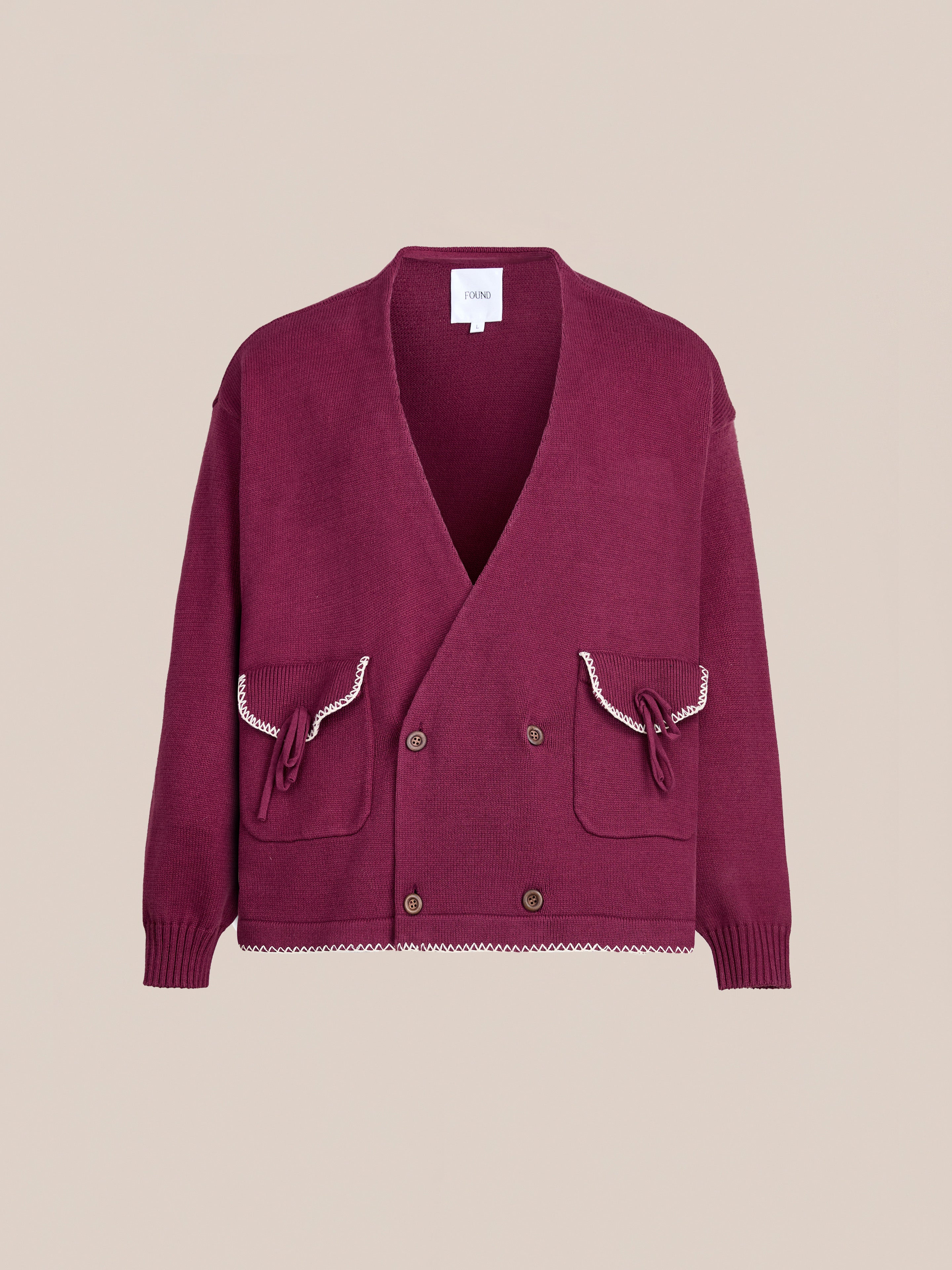 The FOUND Double Breasted Bow Cardigan is a maroon unisex knit with a relaxed fit, two front pockets, button closures, and decorative trim on the pockets and hem, shown against a plain background.