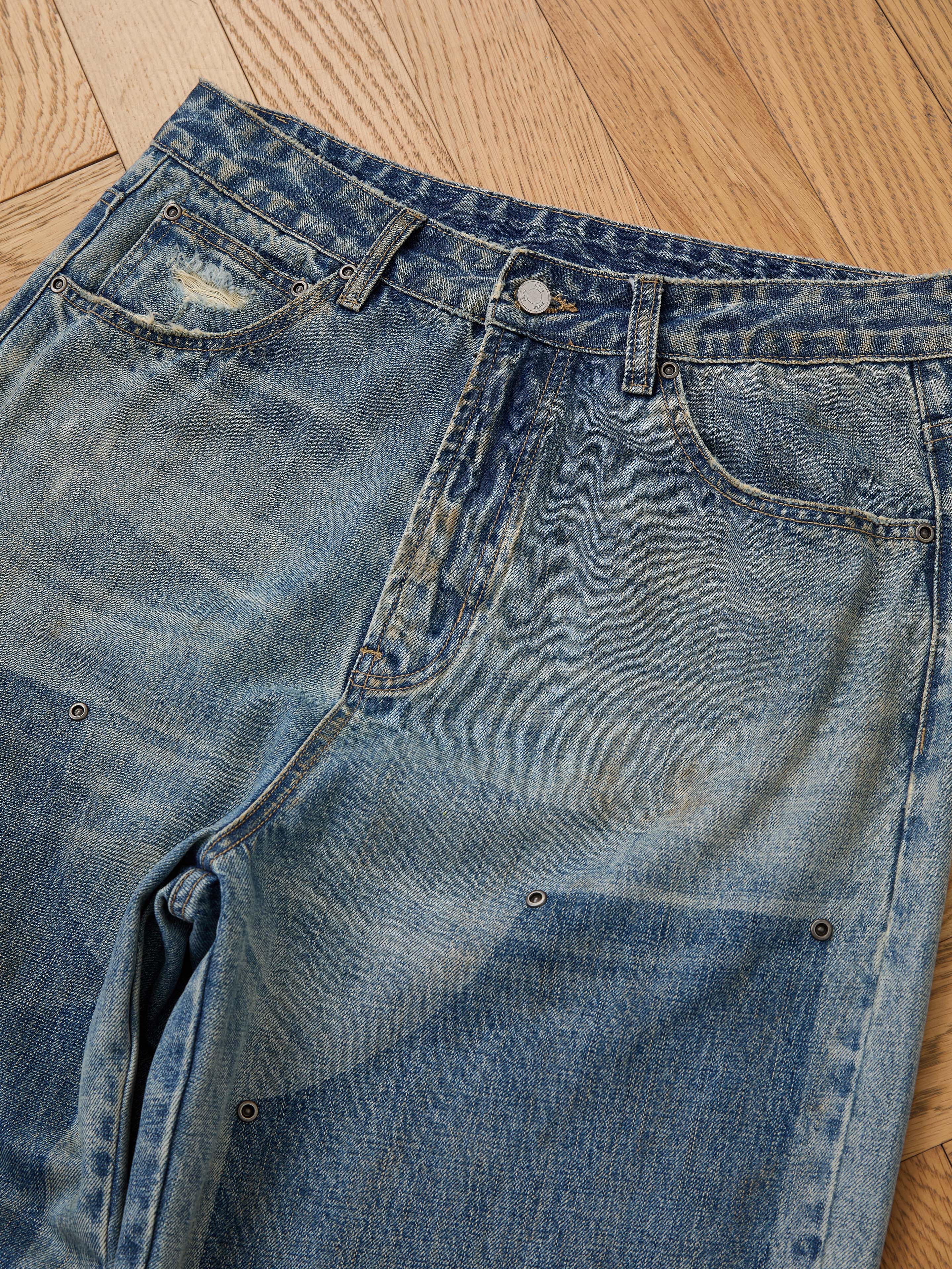 The FOUND Double Knee Carpenter Jeans feature a vintage wash with faded and distressed details, metal rivets, and visible wear, shown laid flat on a wooden floor.