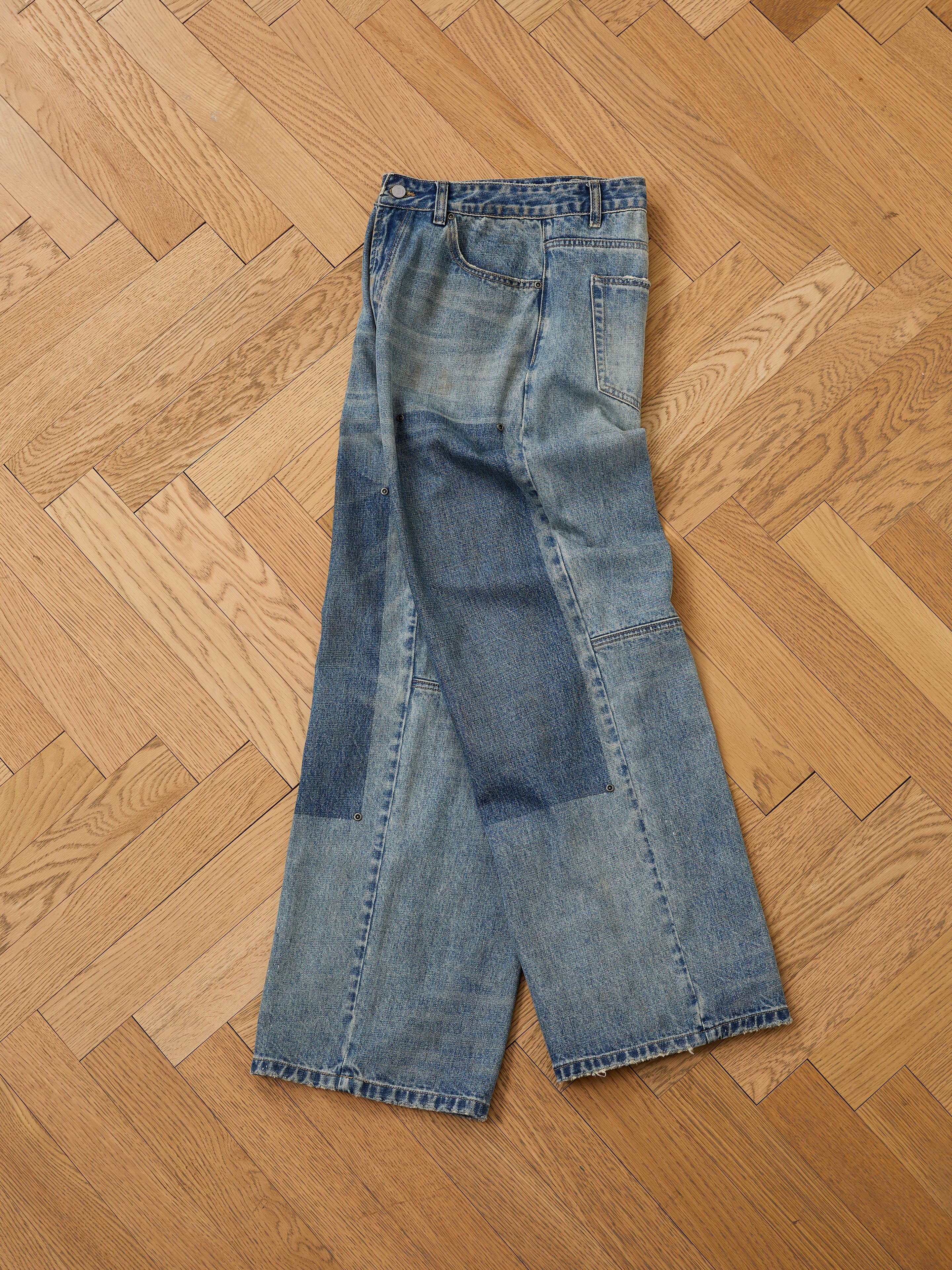FOUND Double Knee Carpenter Jeans featuring a vintage wash with visible patches and repairs, displayed flat on a light wood herringbone floor.