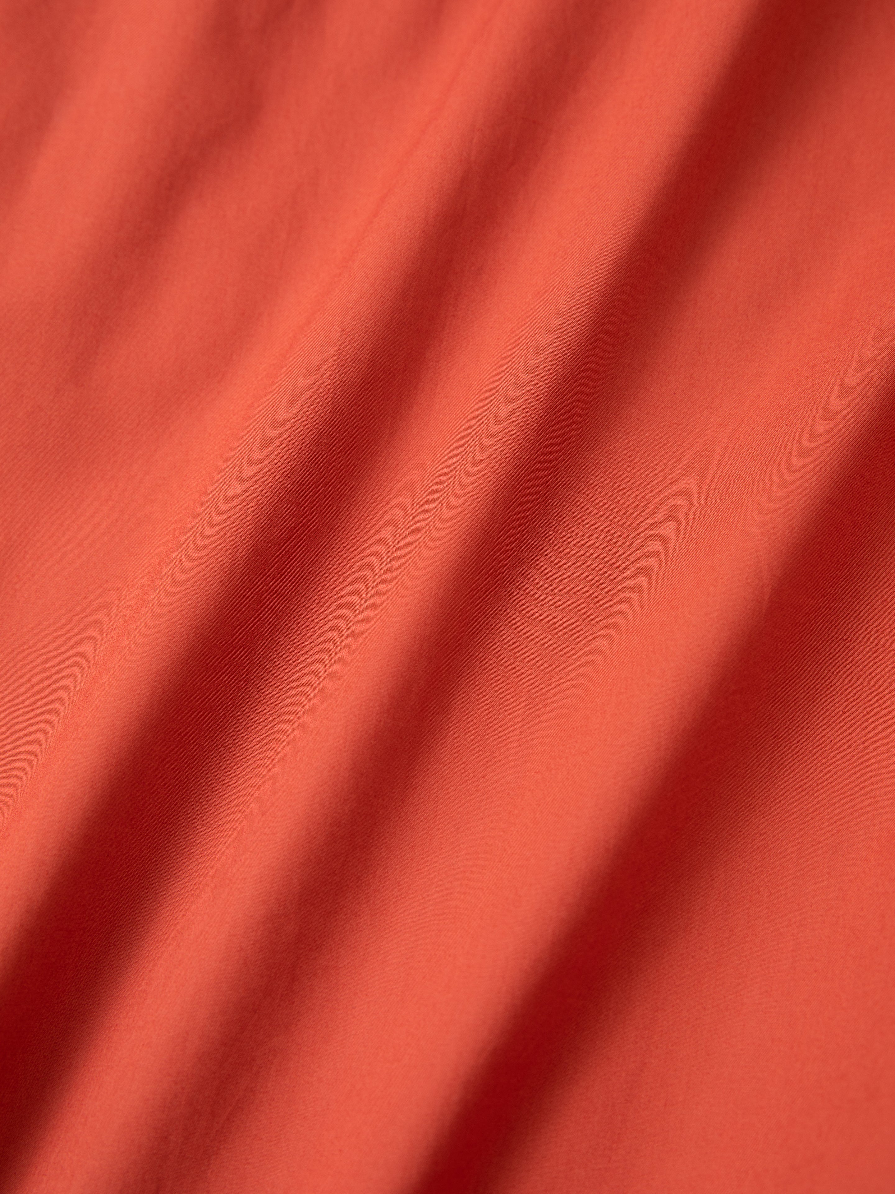Close-up of the Embroidered Western Button Up by FOUND showcasing its orange fabric with soft folds and subtle shadows, creating a textured appearance.