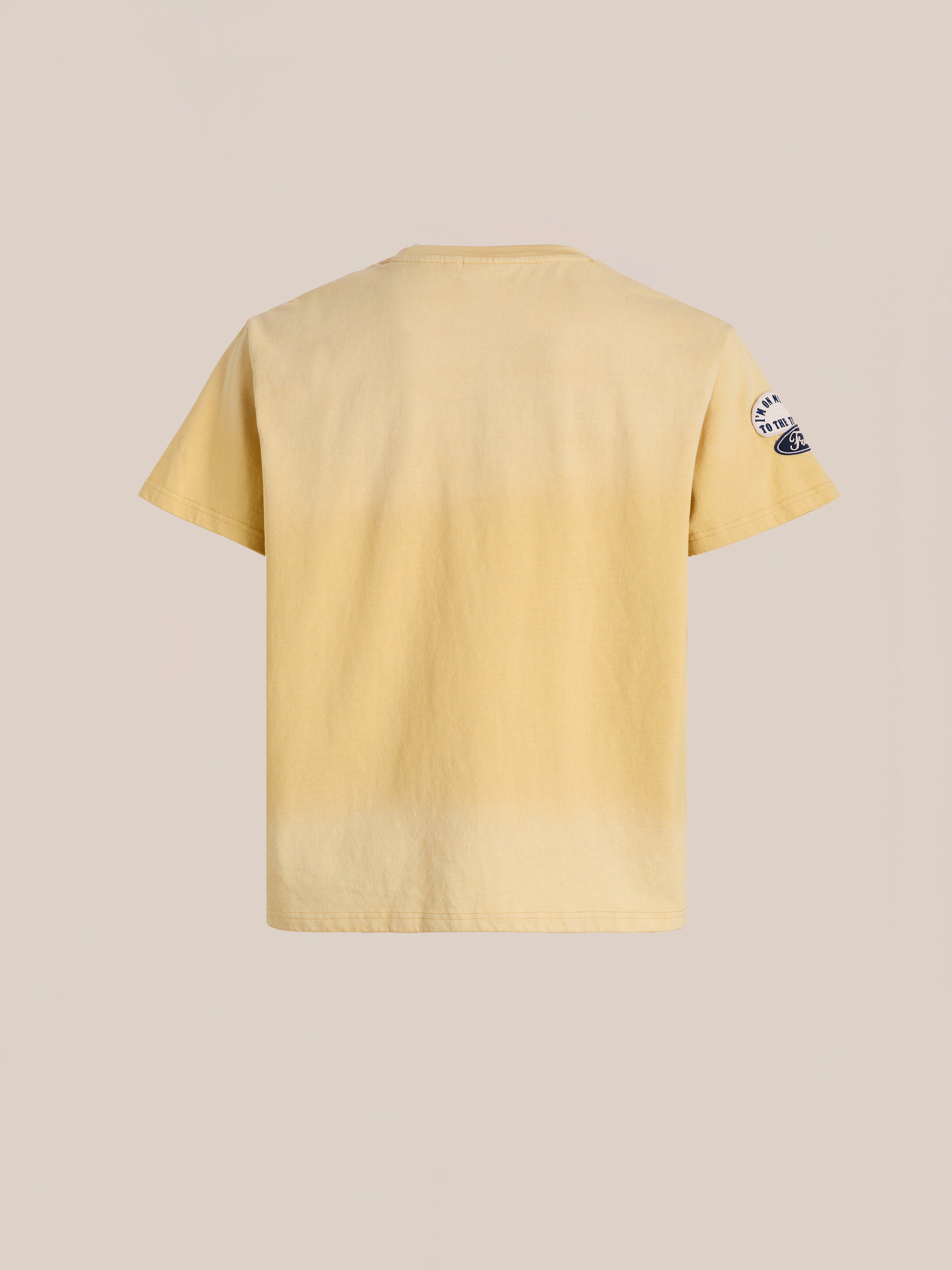 Back view of the FOUND Patchwork Camp Tee, a unisex relaxed fit in plain light yellow short sleeves, featuring a small black and white vintage-inspired embroidered patch on the left sleeve.